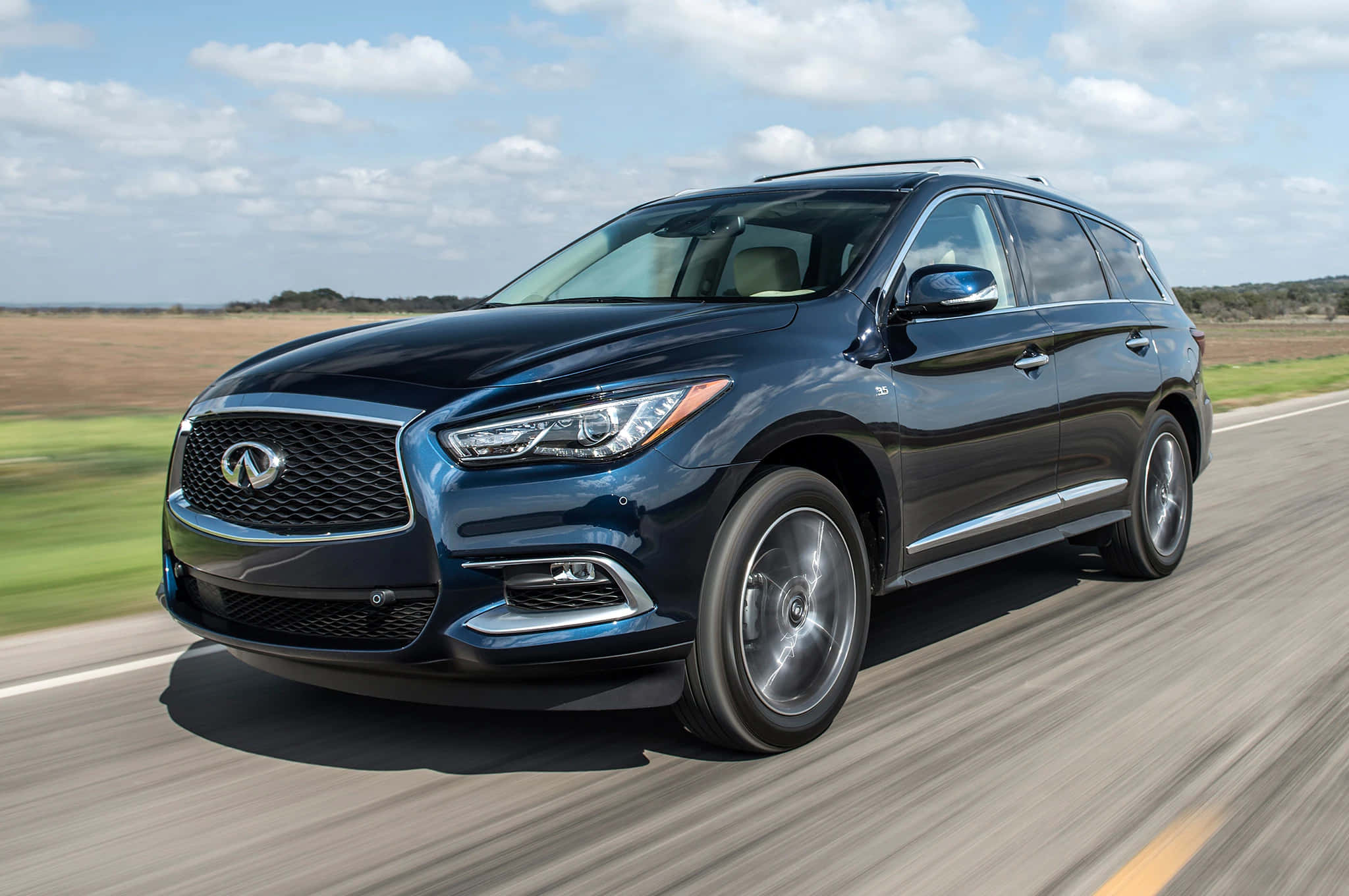 Infiniti Qx60 桌布 壁紙 — 一輛時尚的深藍色 Infiniti SUV 在陽光明媚的高速公路上飛馳，背景是模糊的綠色田野和多雲的天空。