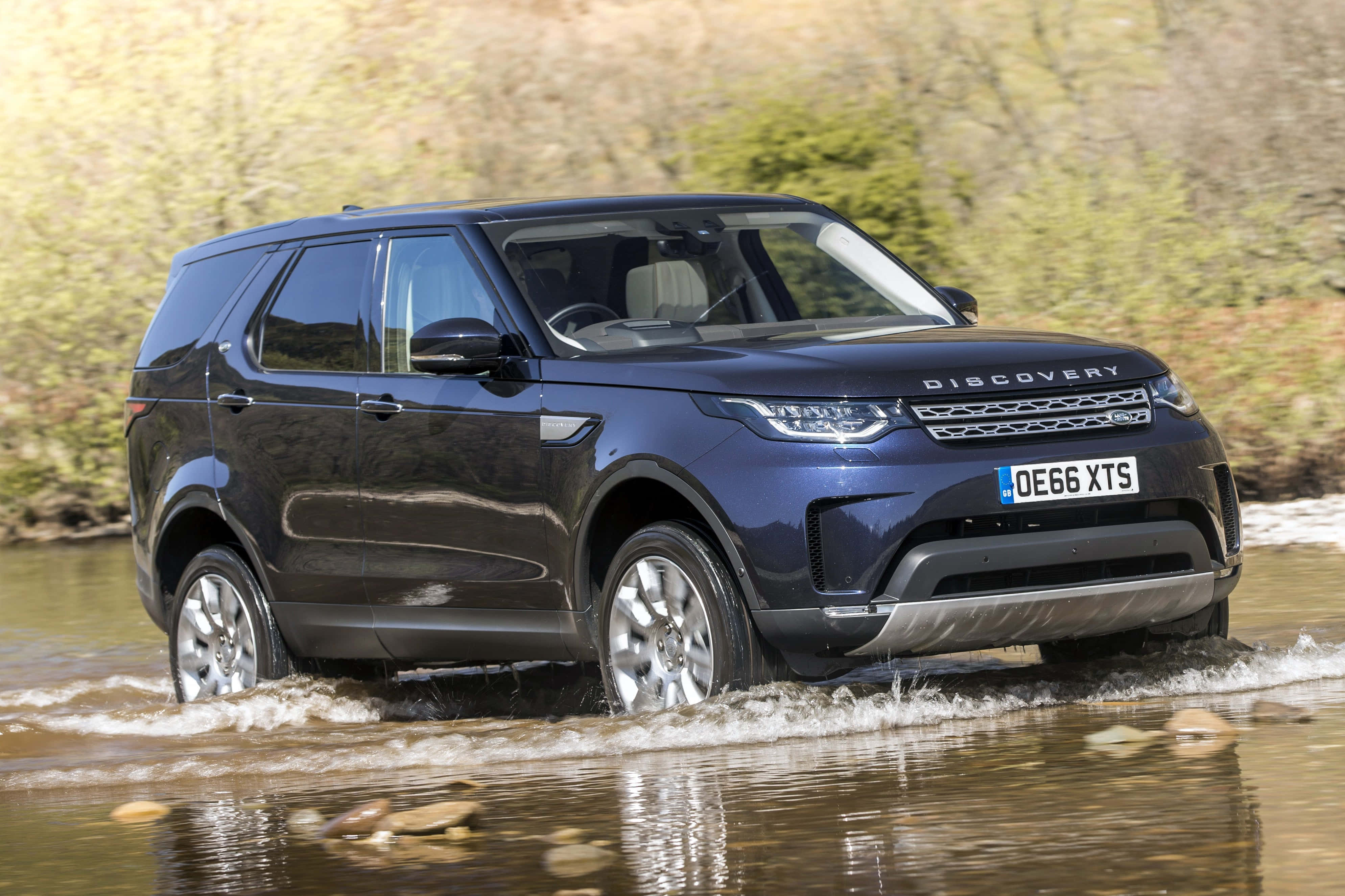 Land Rover Discovery 桌布 壁紙 — 一輛時尚的深藍色 Land Rover Discovery 駛過淺水，水波在車輪周圍飛濺。