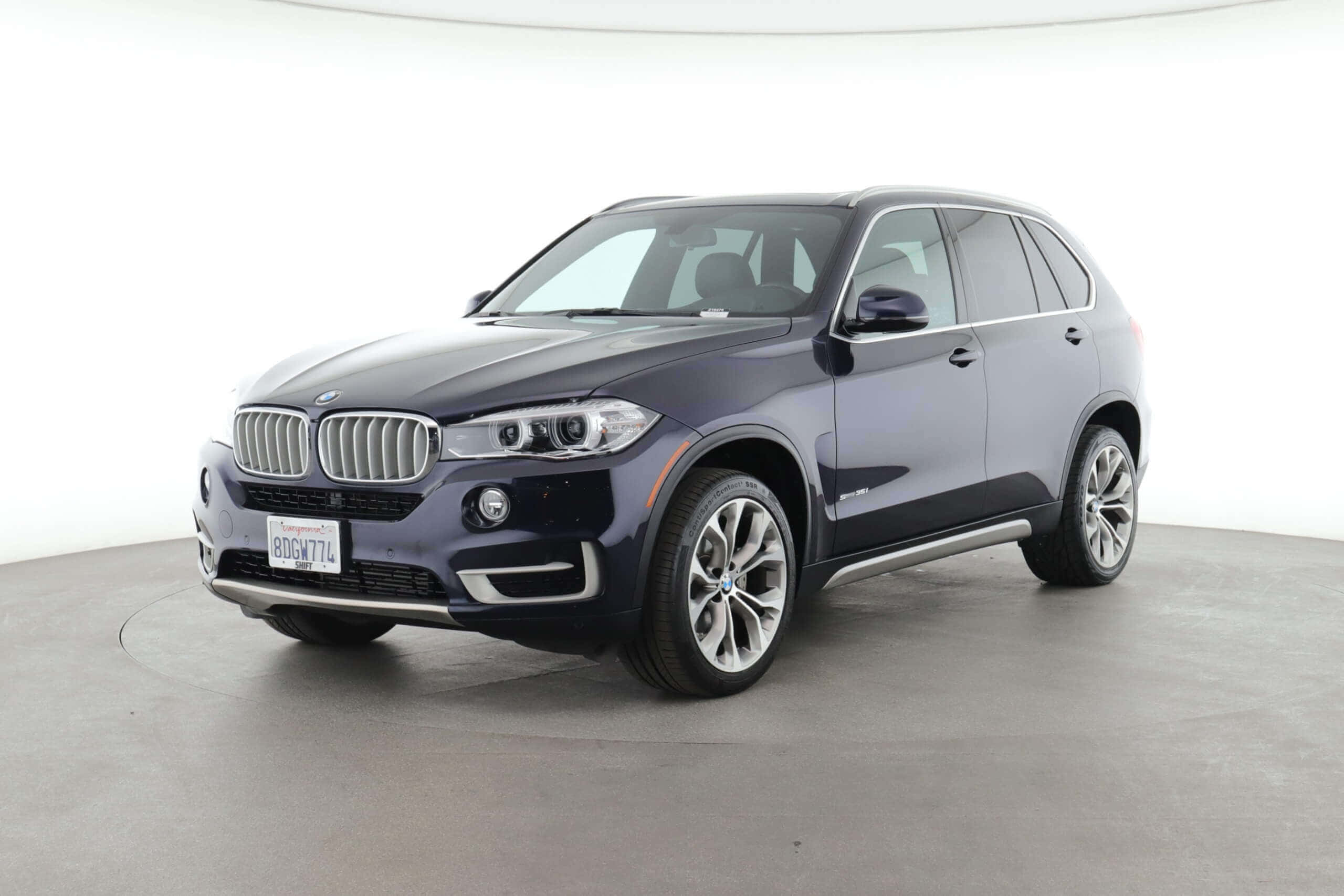 Bmw X5 桌布 壁紙 — 一輛時尚的深藍色BMW X5 SUV在簡約的工作室中展示，配有明亮的白色牆壁和灰色地板。