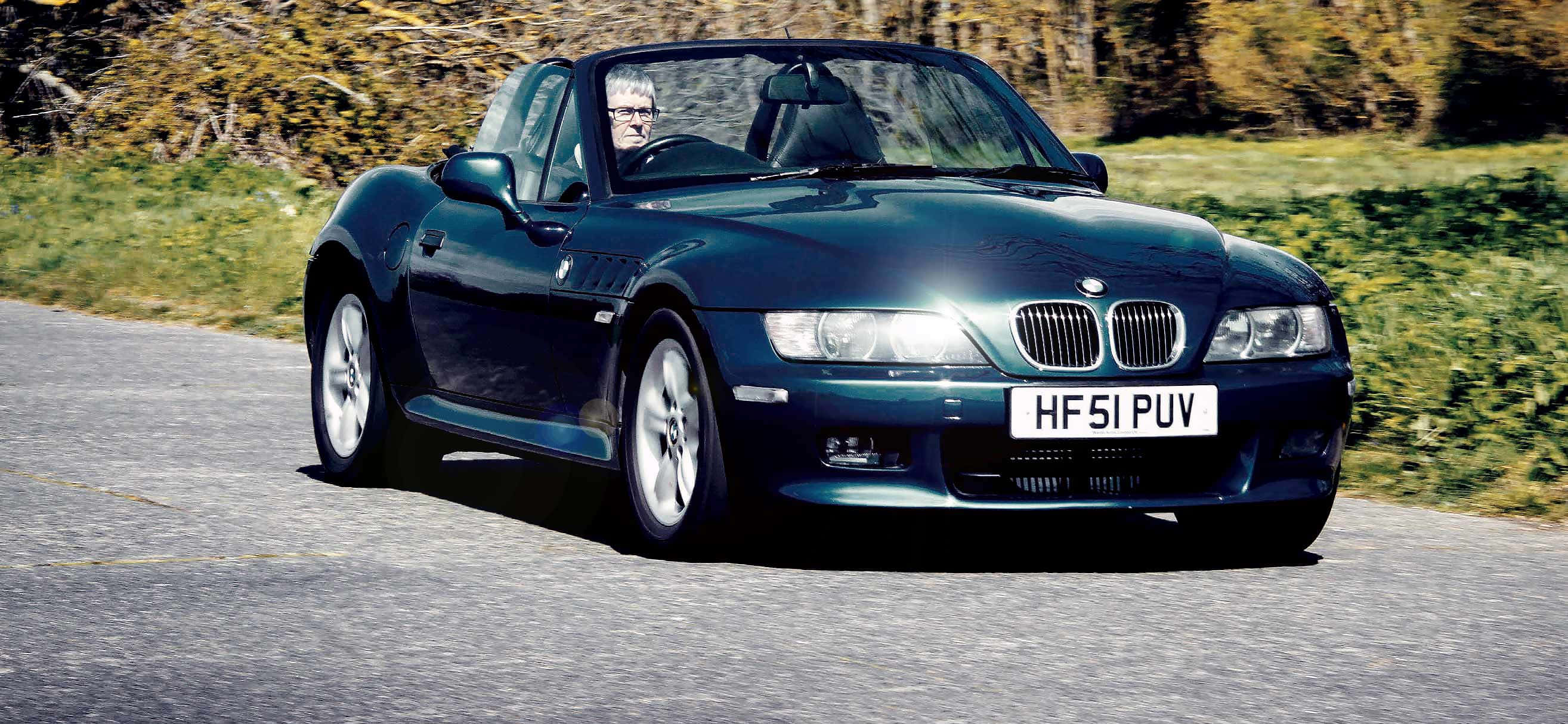 Bmw Z3 桌布 壁紙 — 一輛時尚的深藍色BMW Z8開篷跑車沿著蜿蜒的鄉村道路行駛，背景是秋天的樹葉。