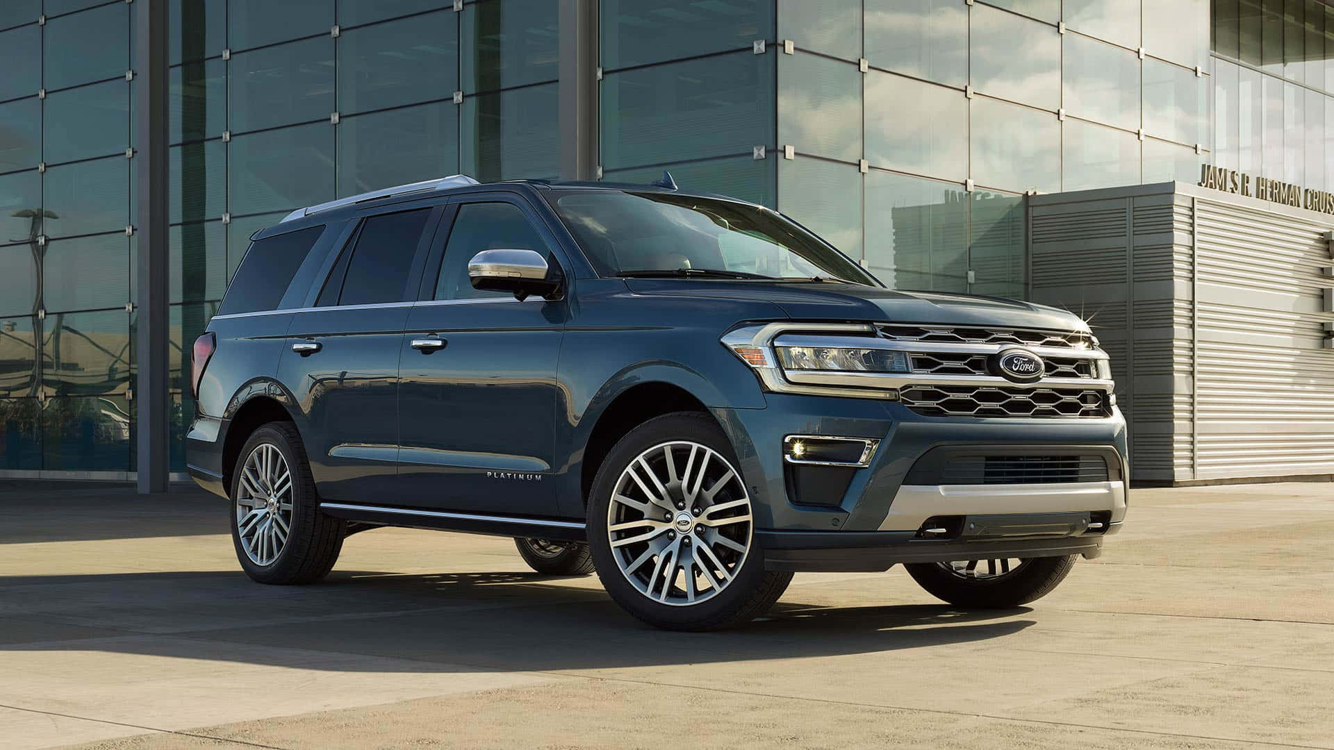 Ford Expedition 桌布 壁紙 — 一輛時尚的深藍色Ford Expedition Platinum SUV在明亮的日光下停泊在現代玻璃建築前。