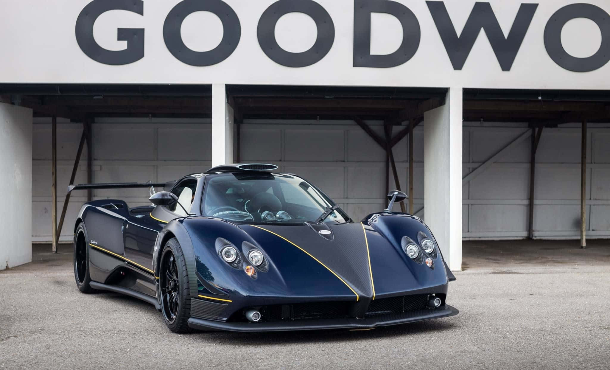 Pagani Zonda C12 Roadster 桌布 壁紙 — 一輛時尚的深藍色Pagani Zonda跑車帶有黃色點綴，停在'GOODWOOD'標誌前。