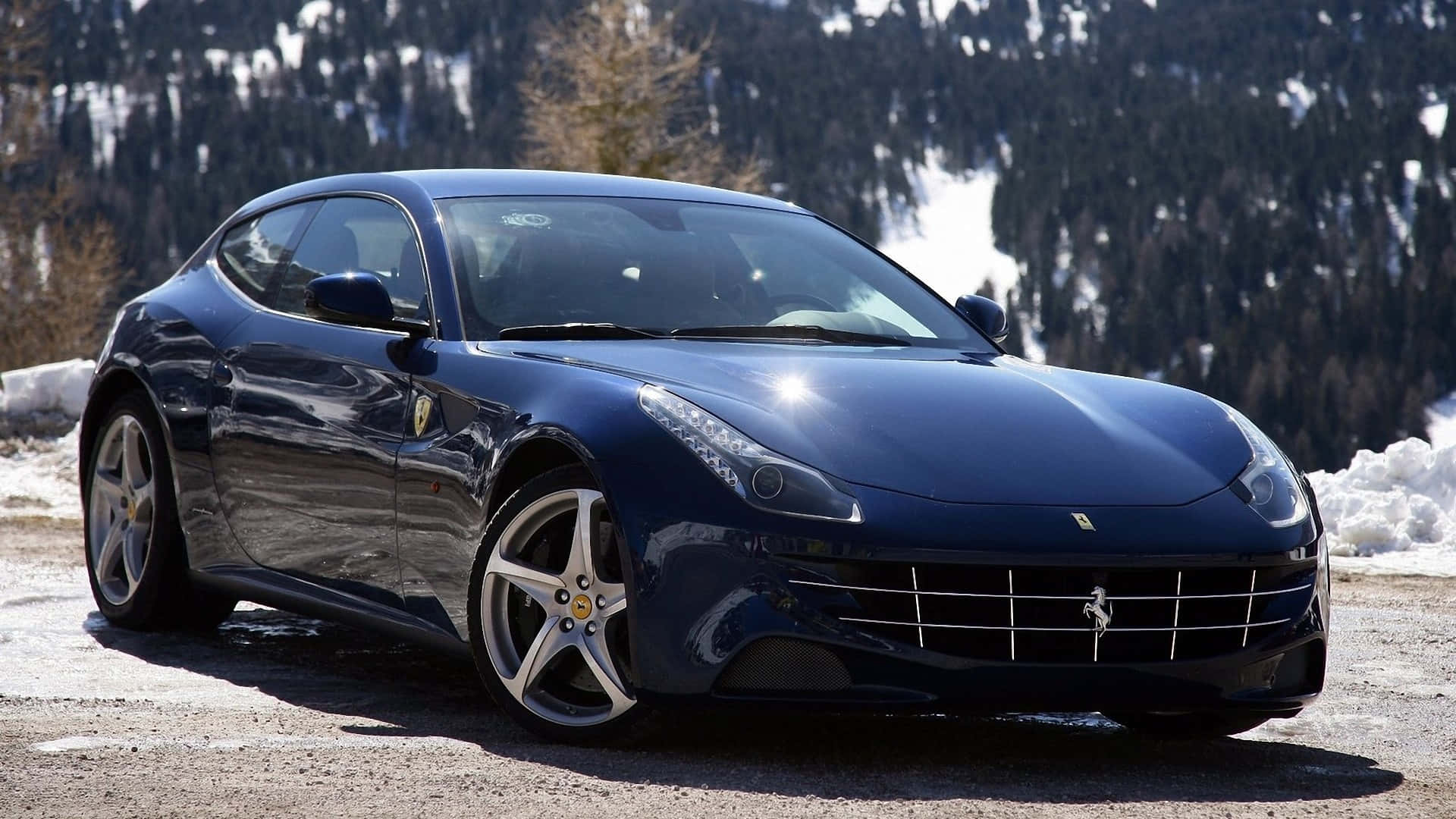 Ferrari Ff 桌布 壁紙 — 一輛時尚的深藍色法拉利跑車在明亮的陽光下閃閃發光，停在白雪覆蓋的山路上，背景有松樹。