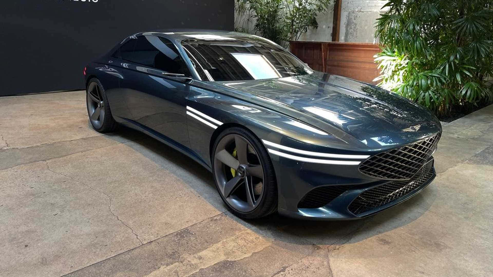 Genesis X Concept 桌布 壁紙 — 一輛時尚的深藍色跑車帶有發光的白色條紋，停在石鋪路面上，旁邊是茂密的綠植。