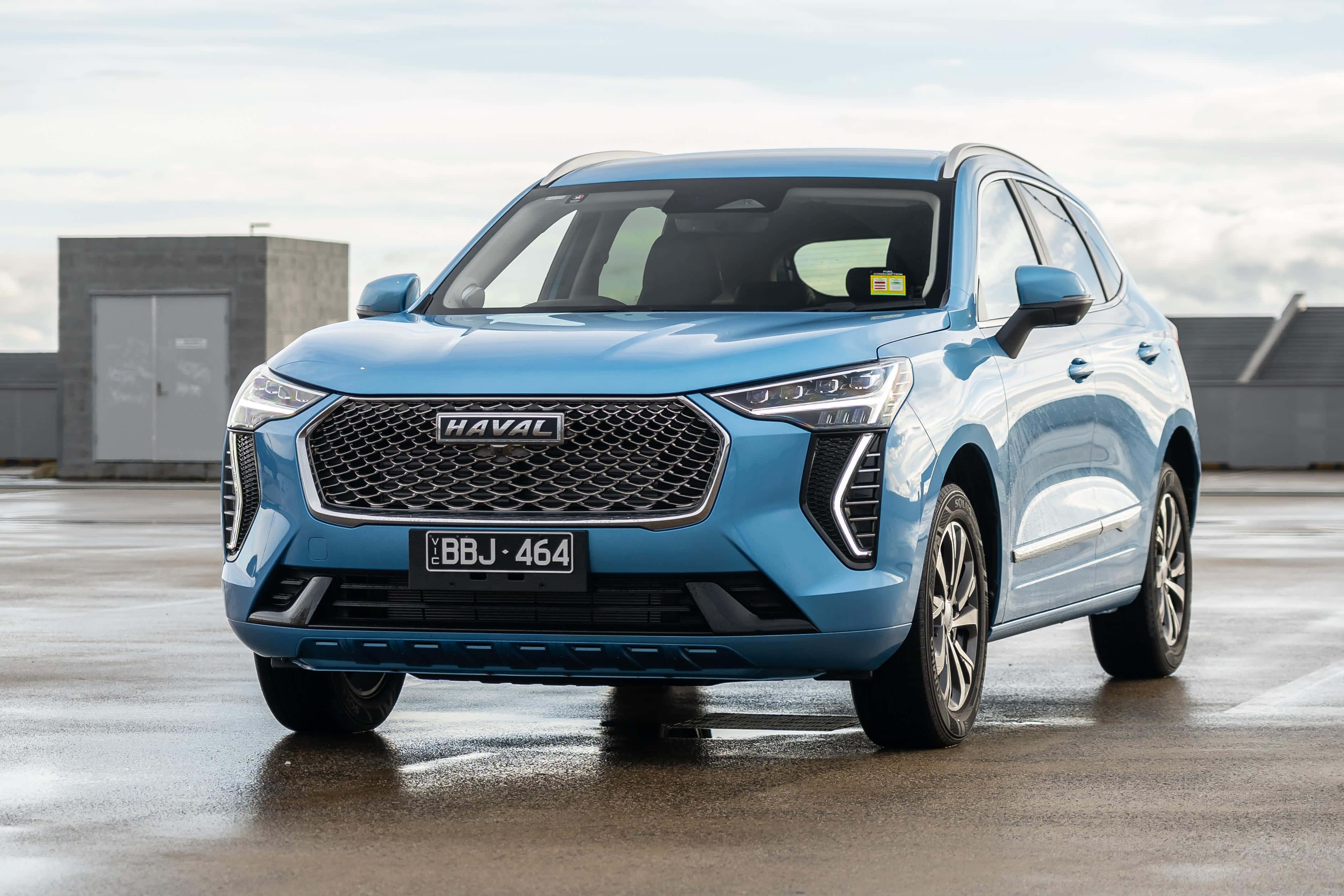 Haval 桌布 壁紙 — 一輛時尚的淺藍色哈弗SUV停泊在濕漉漉的混凝土表面上，背景是現代工業建築，天空多雲。