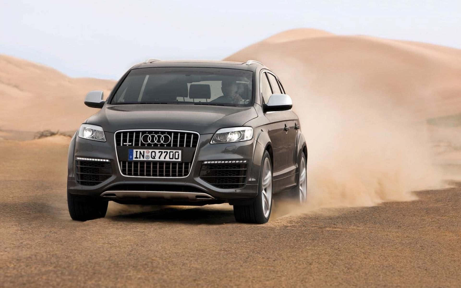 Audi Q7 桌布 壁紙 — 一輛時尚的灰色Audi Q7 SUV在明亮的白天場景中穿過沙漠沙丘，揚起沙塵。