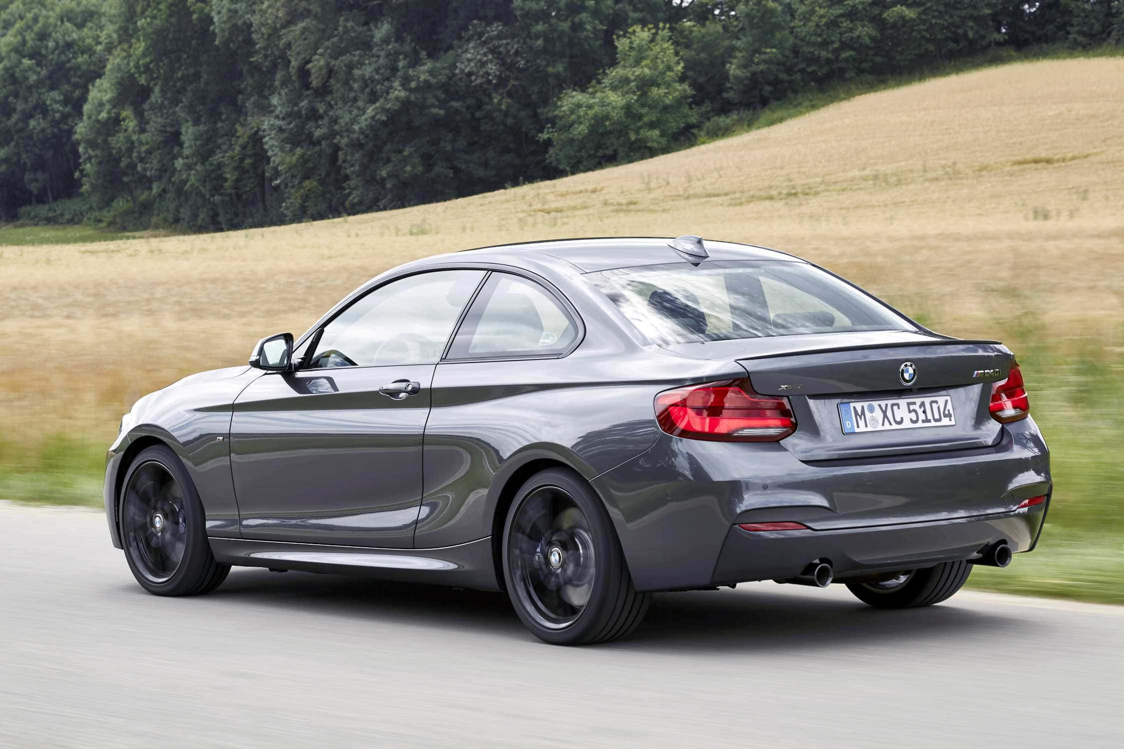 Bmw 2 Series 桌布 壁紙 — 一輛時尚的灰色BMW M2雙門跑車在鄉間道路上疾馳，背景是模糊的金色田野和綠樹。