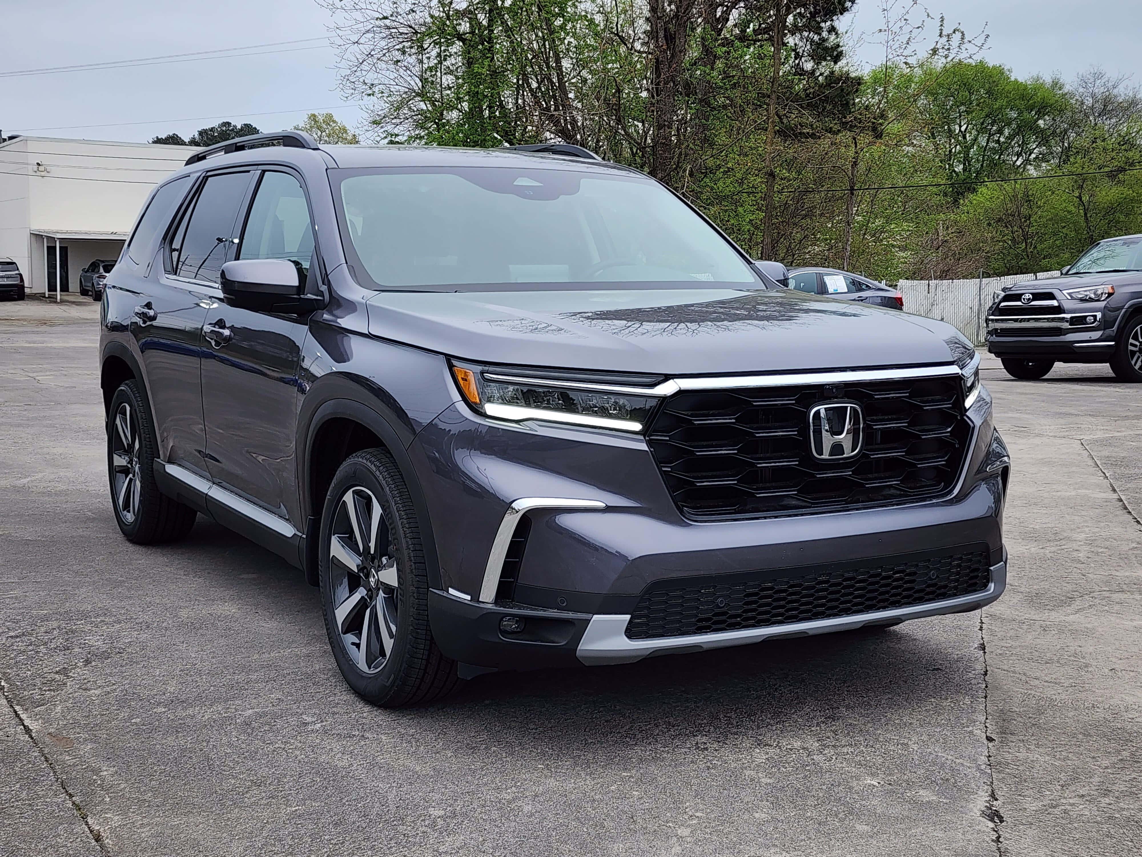 Honda Pilot 桌布 壁紙 — 一輛時尚的灰色本田Pilot SUV停放在混凝土停車場上，背景有樹木和其他車輛。