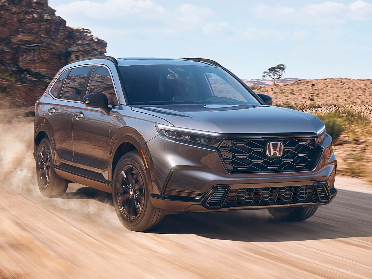Honda Hr-v 桌布 壁紙 — 一輛時尚的灰色本田SUV在明亮的藍天下，在塵土飛揚的沙漠景觀中疾馳，揚起沙塵。