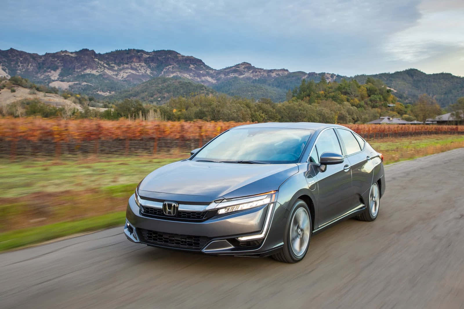 Honda Clarity 桌布 壁紙 — 一輛時尚的灰色本田轎車沿著蜿蜒的道路疾馳，背景是模糊的秋葉和崎嶇的山脈。