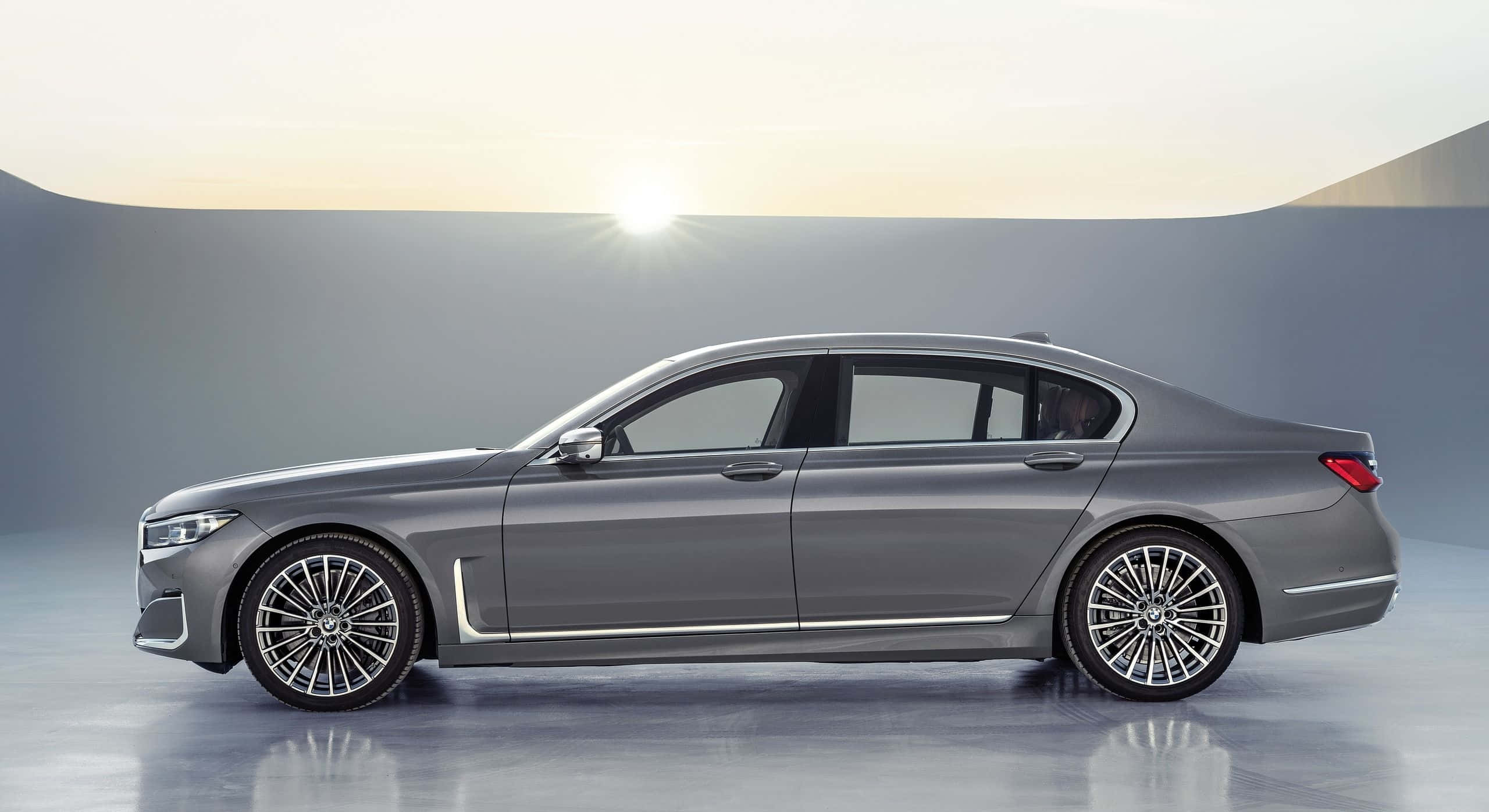 Bmw 7 Series 桌布 壁紙 — 一輛時尚的灰色豪華轎車在極簡工作室背景下以側面展示，背景有發光的太陽。
