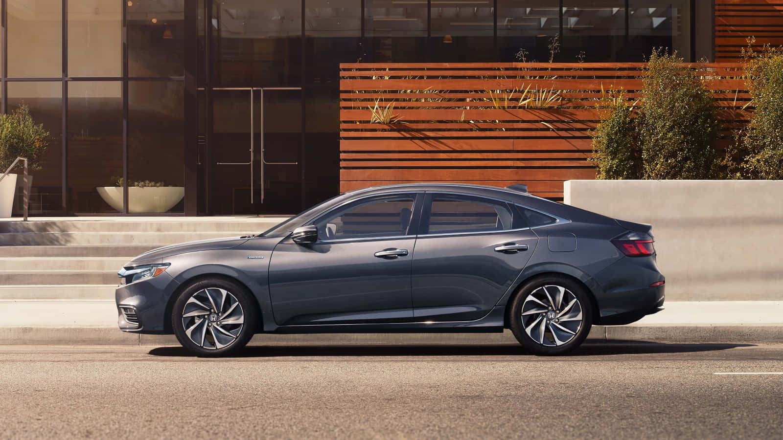 Honda Insight 桌布 壁紙 — 一輛時尚的灰色轎車停泊在城市街道上，旁邊是一座帶有玻璃窗和木條的現代建築。