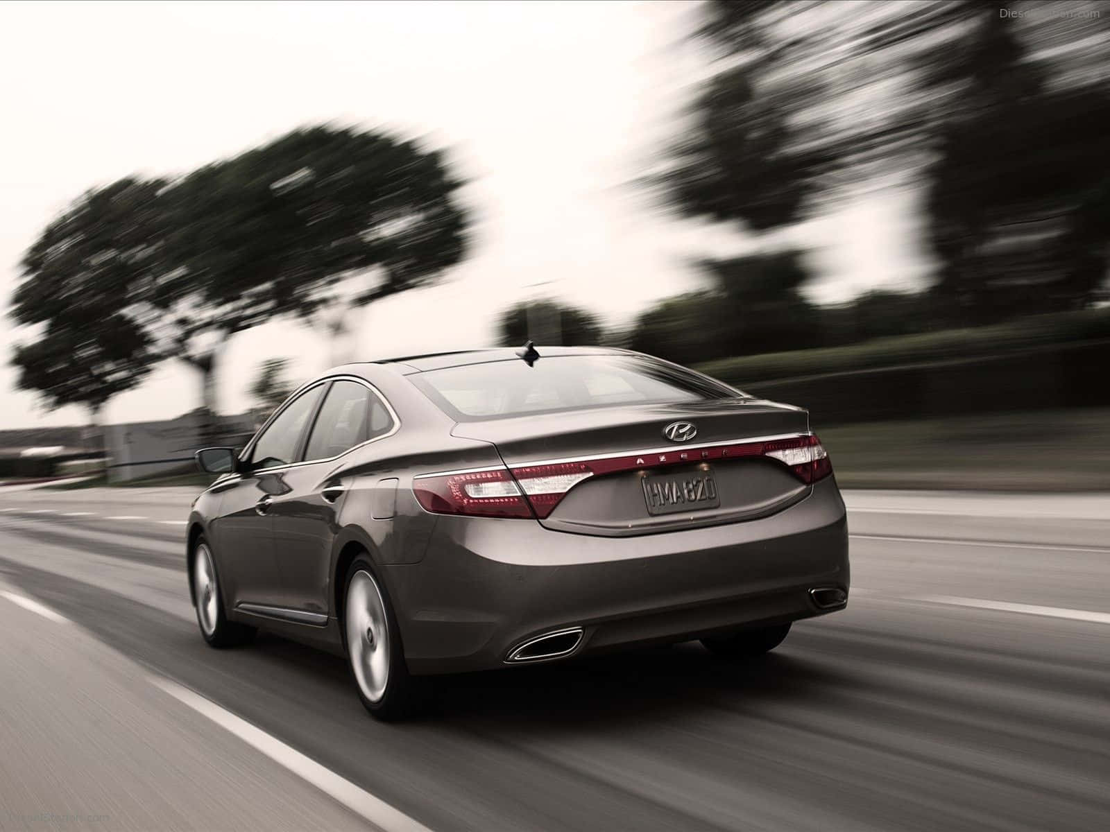 Hyundai Azera 桌布 壁紙 — 一輛時尚的灰色轎車在高速公路上飛馳，模糊的樹木和天空傳達出運動感和現代設計。