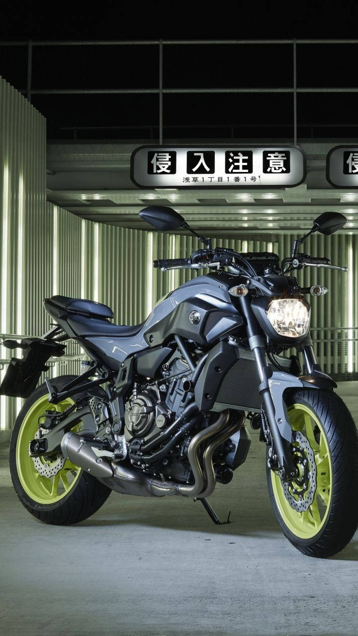 yamaha mt 15 桌布 壁紙 — 一輛時尚的灰色電單車，配備螢光綠色車輪，夜晚停泊在現代工業車庫中發光的標誌下。