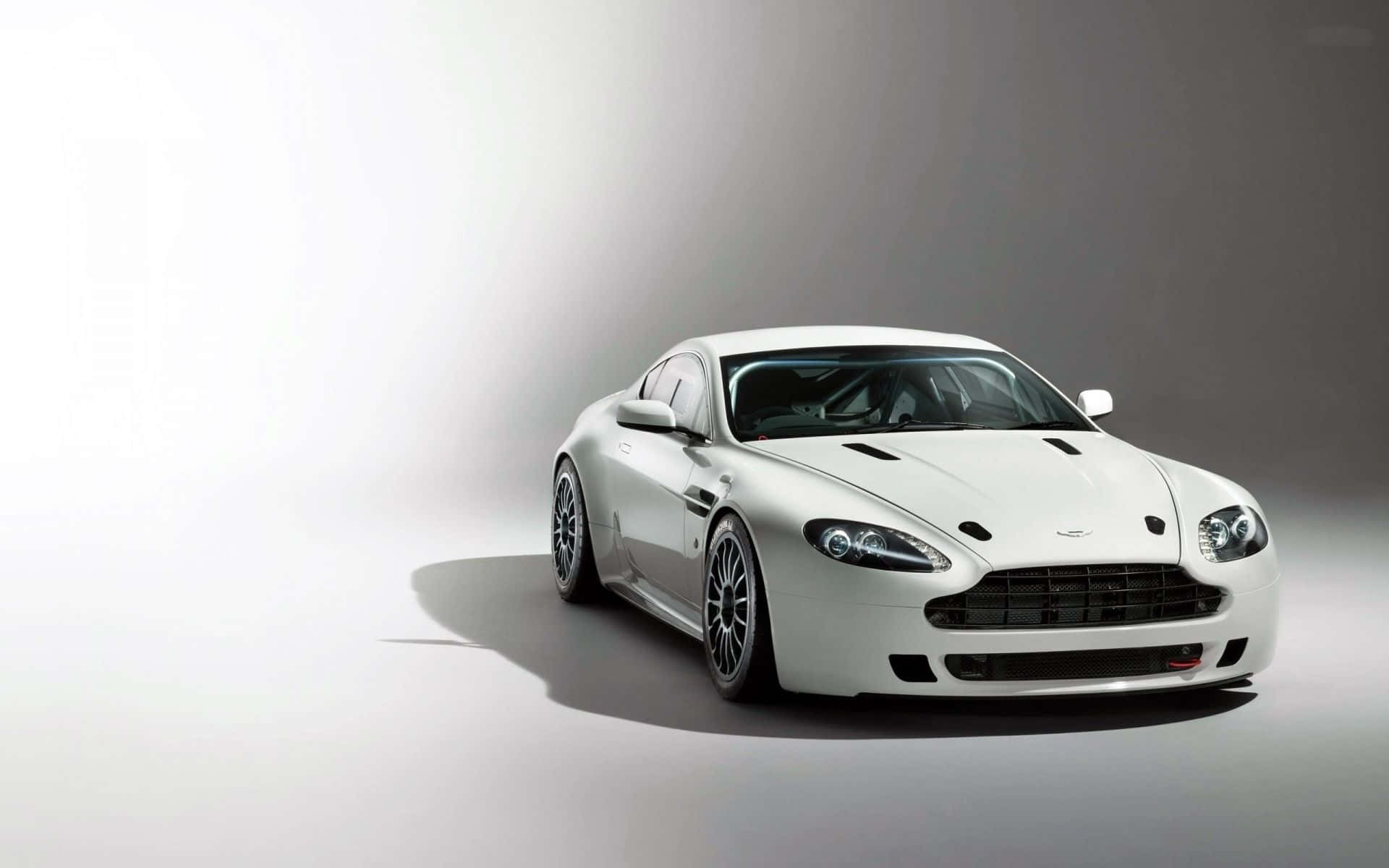 Aston Martin V12 Vantage 桌布 壁紙 — 一輛時尚的白色Aston Martin跑車在攝影棚燈光下，以極簡灰色漸變背景襯托，閃耀光芒。