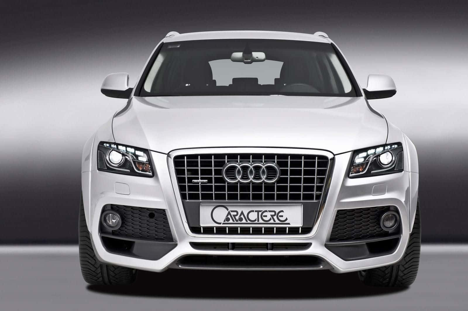 Audi Sq5 桌布 壁紙 — 一輛時尚的白色Audi SUV，配備定製的Caractere鬼面罩和進取式頭燈，在漸變灰色工作室背景前凝視前方。