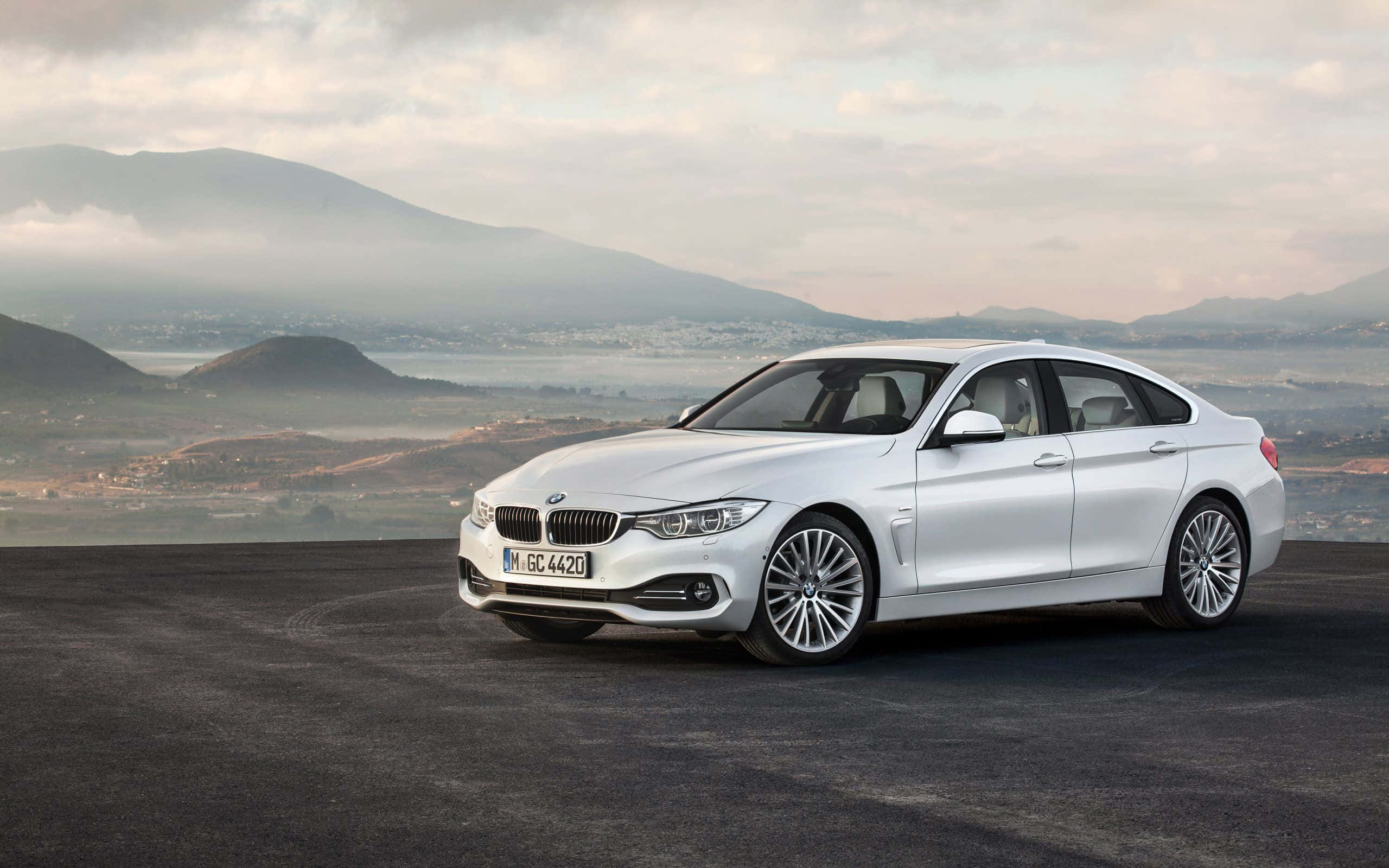Bmw 4 Series 桌布 壁紙 — 一輛時尚的白色BMW 4系轎跑車停在一個黑暗的觀景點，背景是霧氣繚繞的山脈和山谷，天空多雲。