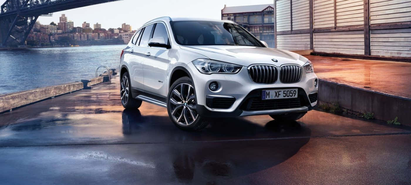 Bmw X1 桌布 壁紙 — 一輛時尚的白色BMW X1 SUV停泊在濕潤的城市碼頭上，背景是城市天際線和橋樑。