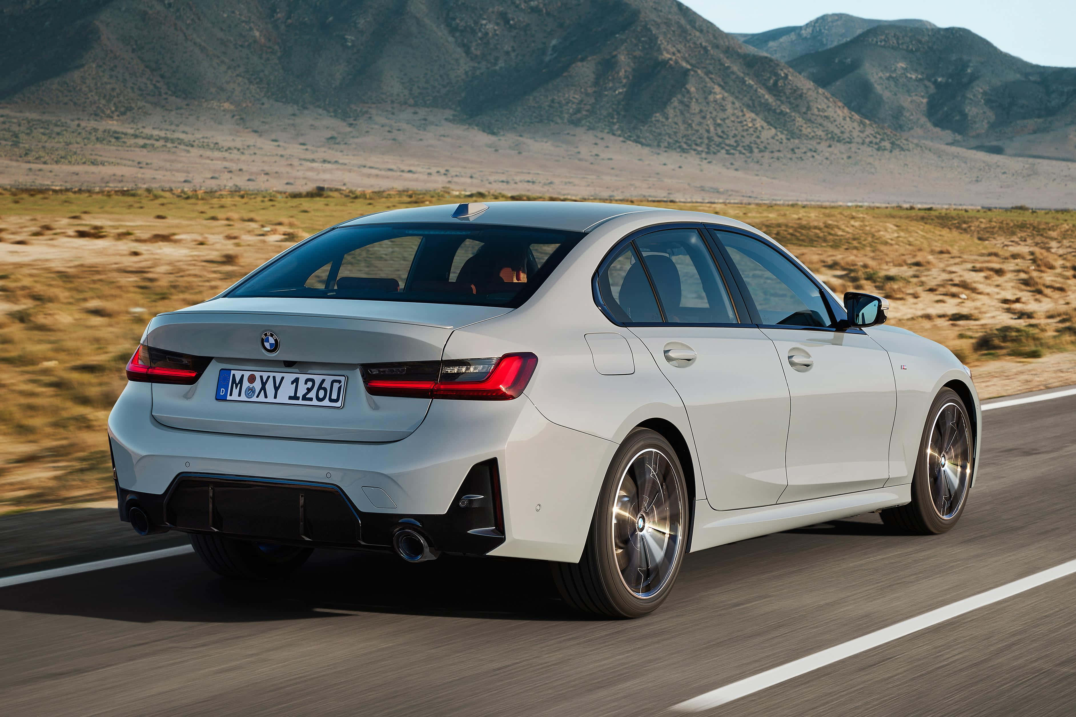 Bmw 3 Series 桌布 壁紙 — 一輛時尚的白色BMW房車在明亮的日光下行駛在沙漠公路上，背景是崎嶇的山脈。