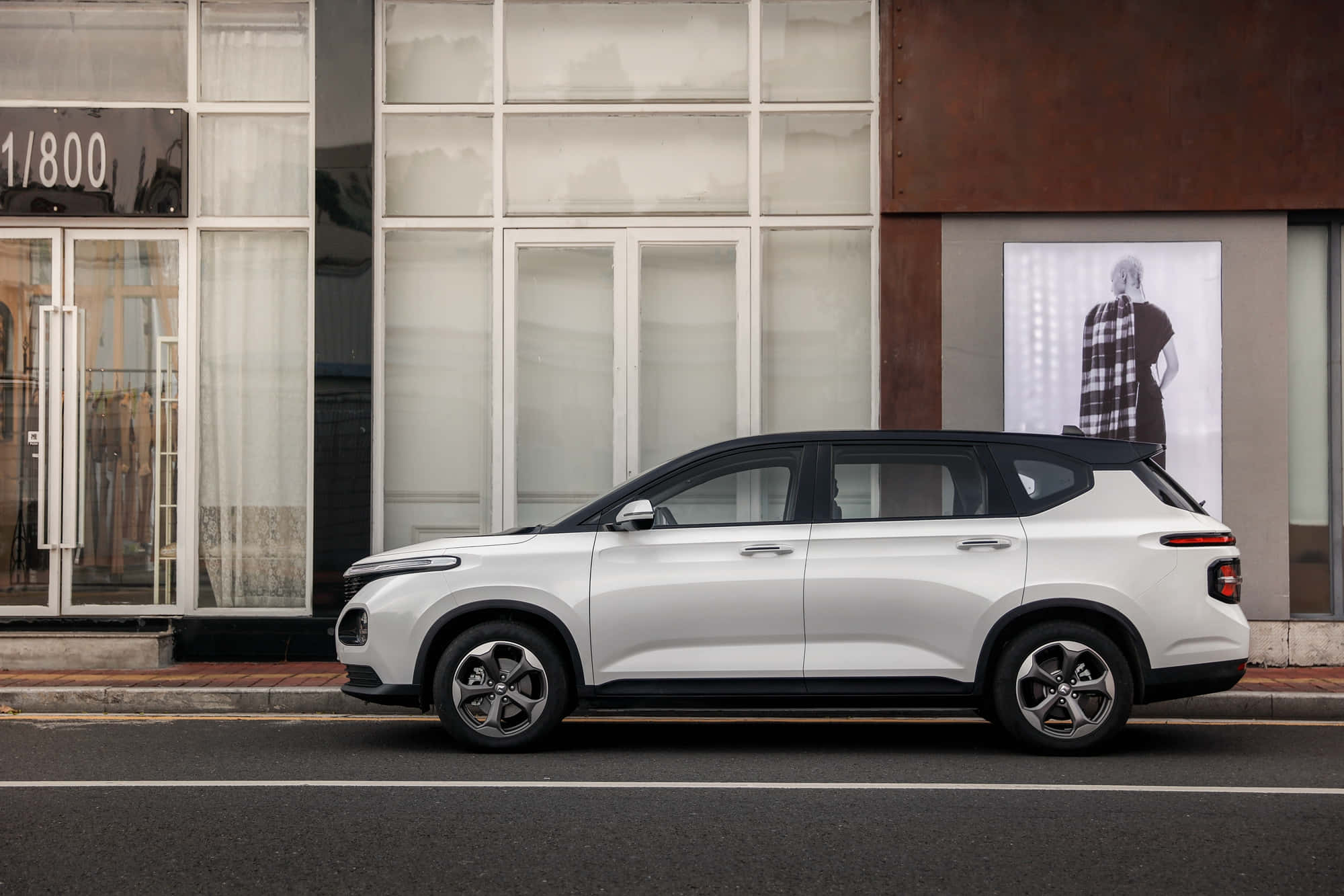 Baojun 桌布 壁紙 — 一輛時尚的白色SUV停泊在城市街道上，旁邊是一座帶有大玻璃窗和時尚海報的現代建築。
