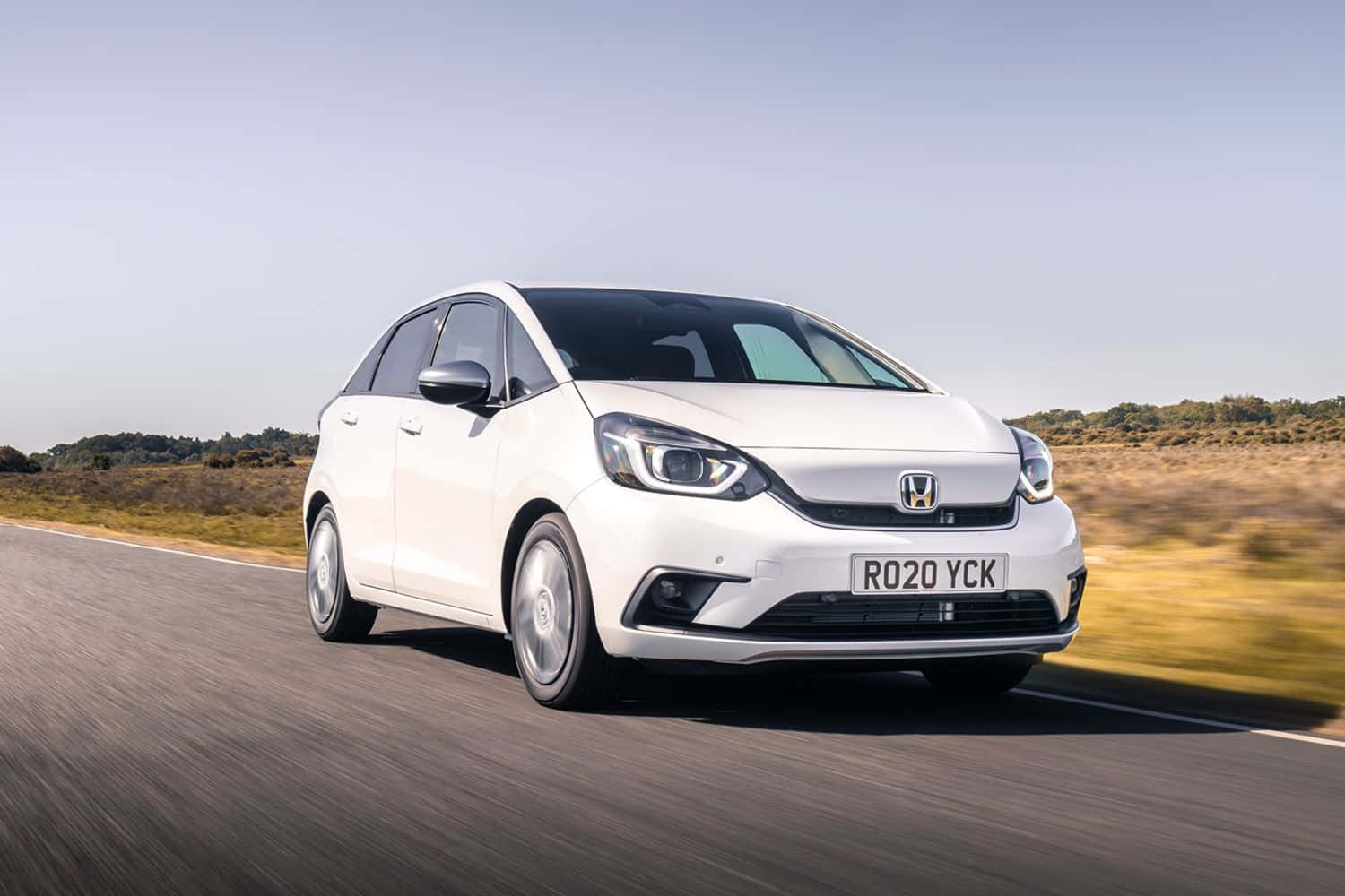 Honda Fit 桌布 壁紙 — 一輛時尚的白色本田Jazz在陽光明媚的鄉村道路上行駛，背景是模糊的動感和金色的草山。
