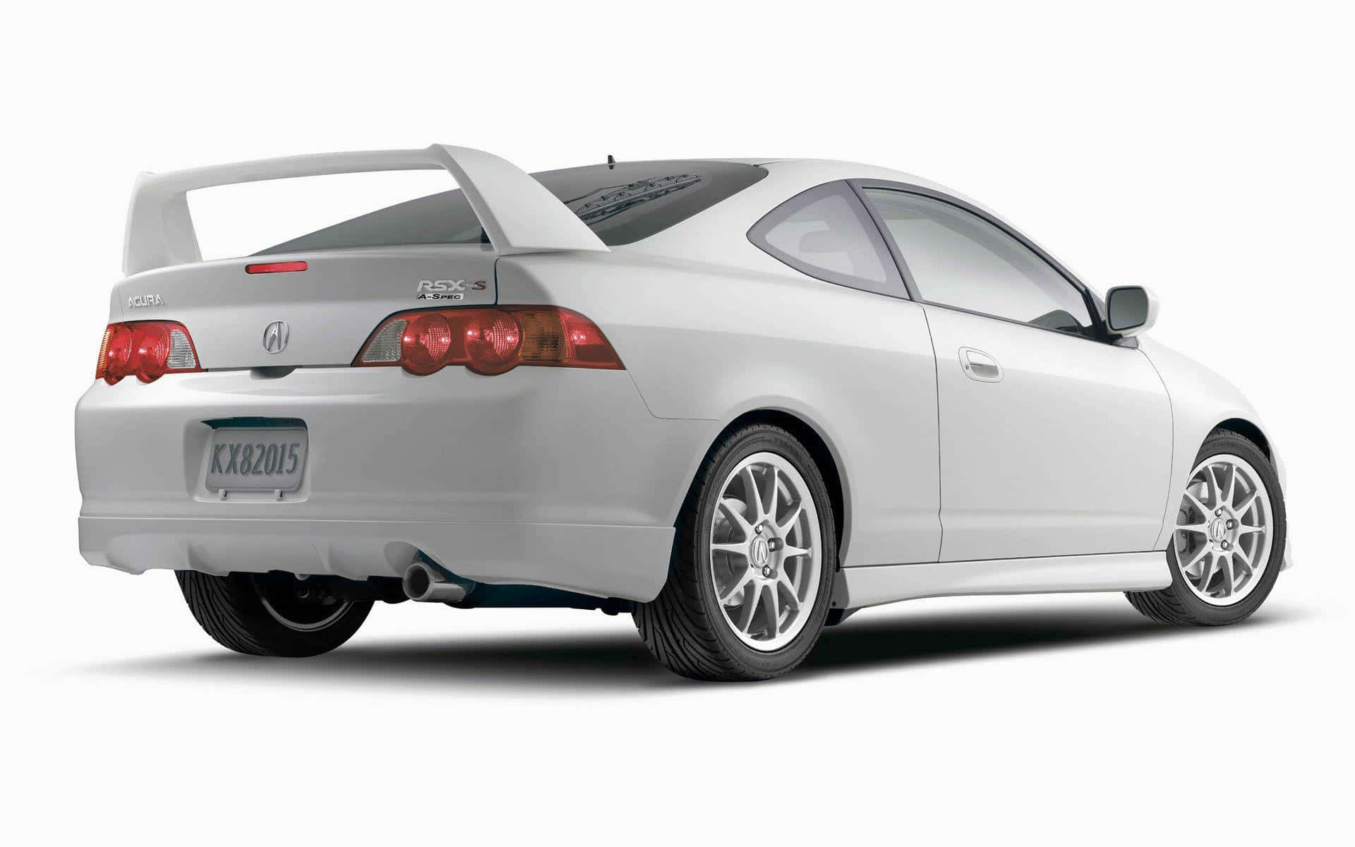 Rsx Type-s 桌布 壁紙 — 一輛時尚的白色本田轎跑車，配備大型後尾翼和紅色尾燈，在攝影棚燈光下展示。