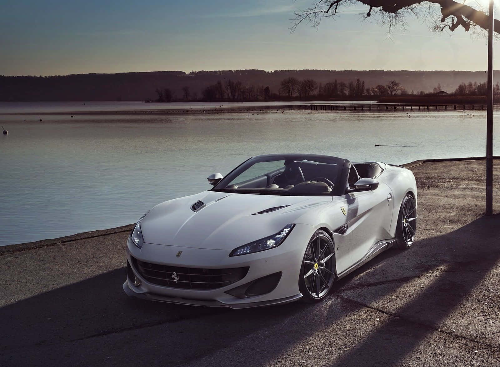 Ferrari Portofino 桌布 壁紙 — 一輛時尚的白色法拉利敞篷車停在寧靜的湖邊，正值黃金時刻，周圍有光禿的樹木和遠山。
