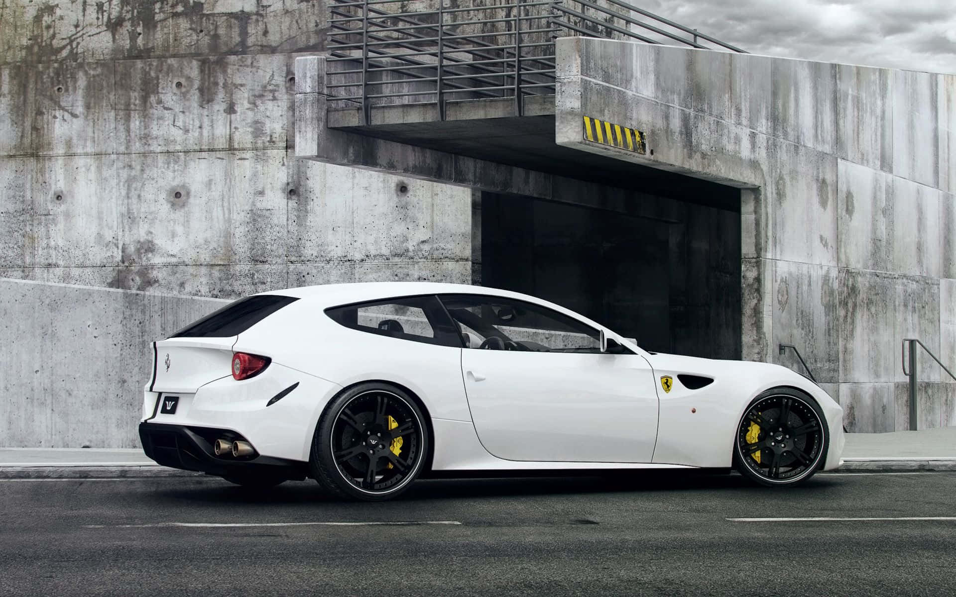 Ferrari Ff 桌布 壁紙 — 一輛時尚的白色法拉利跑車，配備黑色輪圈和黃色點綴，停放在風化的混凝土車庫入口旁。