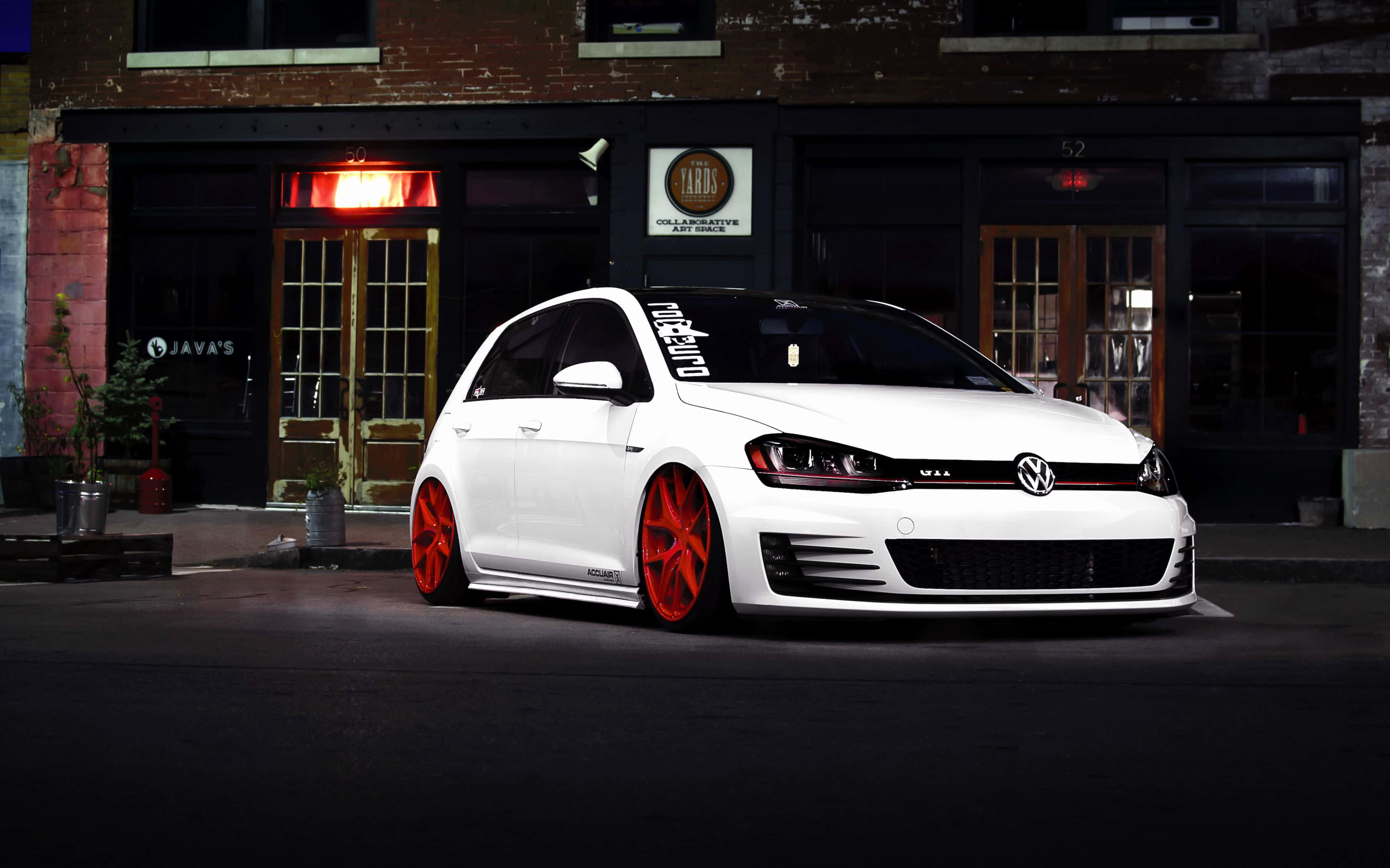 Jdm Car 桌布 壁紙 — 一輛時尚的白色福士Golf配以鮮紅色輪圈，夜間停在一棟帶有發光招牌的磚砌建築前。