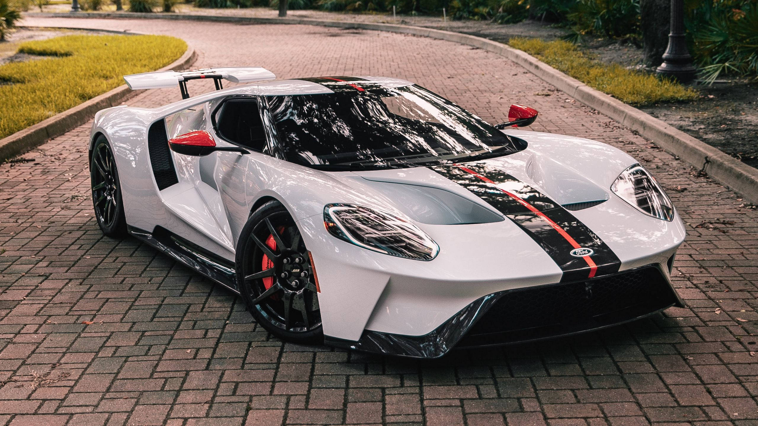 Sports Car 桌布 壁紙 — 一輛時尚的白色福特GT跑車，帶有黑色和紅色點綴，停在磚砌車道上，周圍環繞著綠草和樹木。