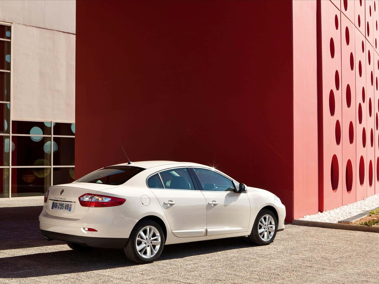 Renault Fluence 桌布 壁紙 — 一輛時尚的白色轎車停放在一面帶有圓形鏤空的醒目紅牆旁，在明亮的日光下。