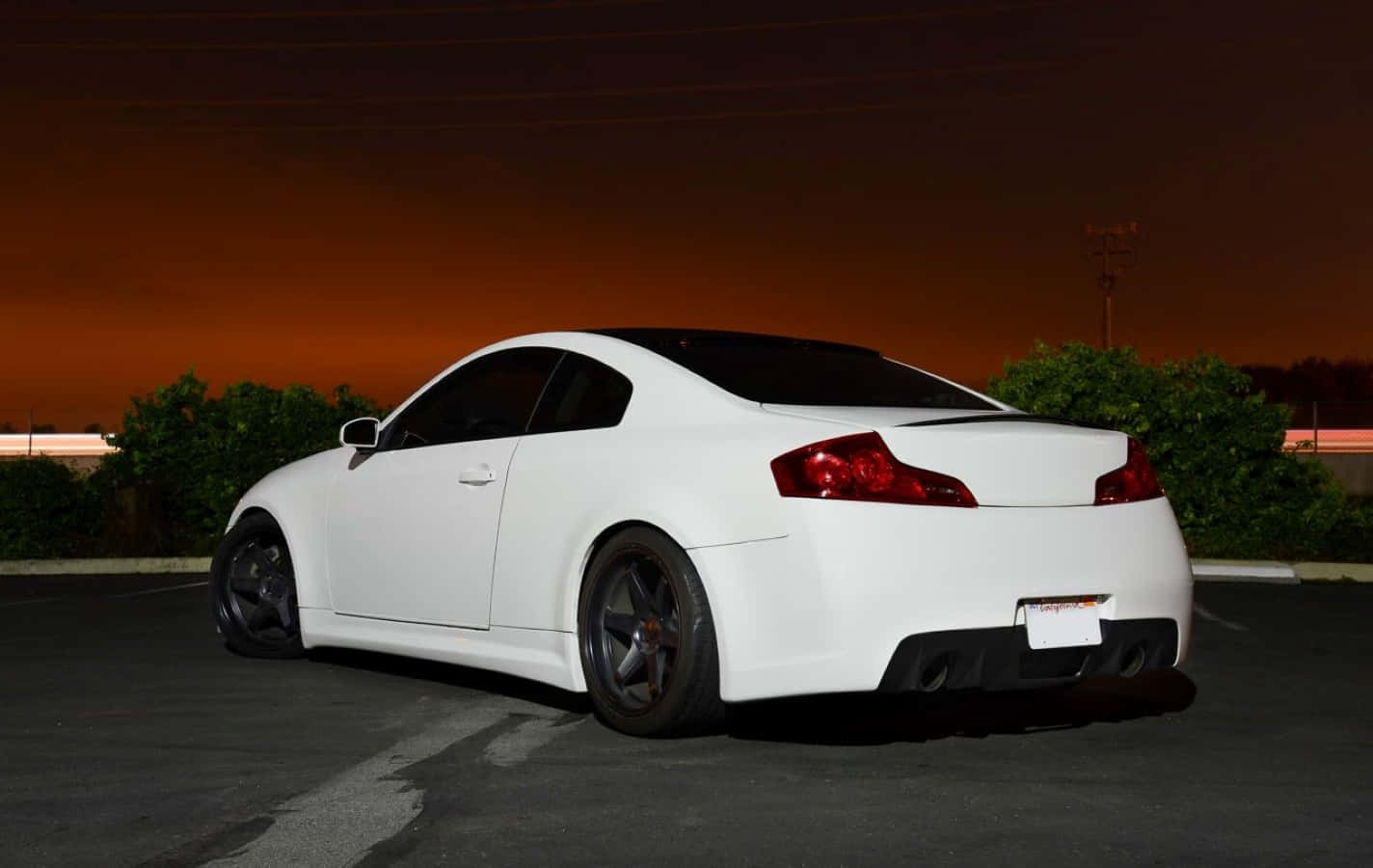 Infiniti G35 桌布 壁紙 — 一輛時尚的白色運動型轎跑車在黃昏時停泊，紅色尾燈在橙色天空下閃爍。
