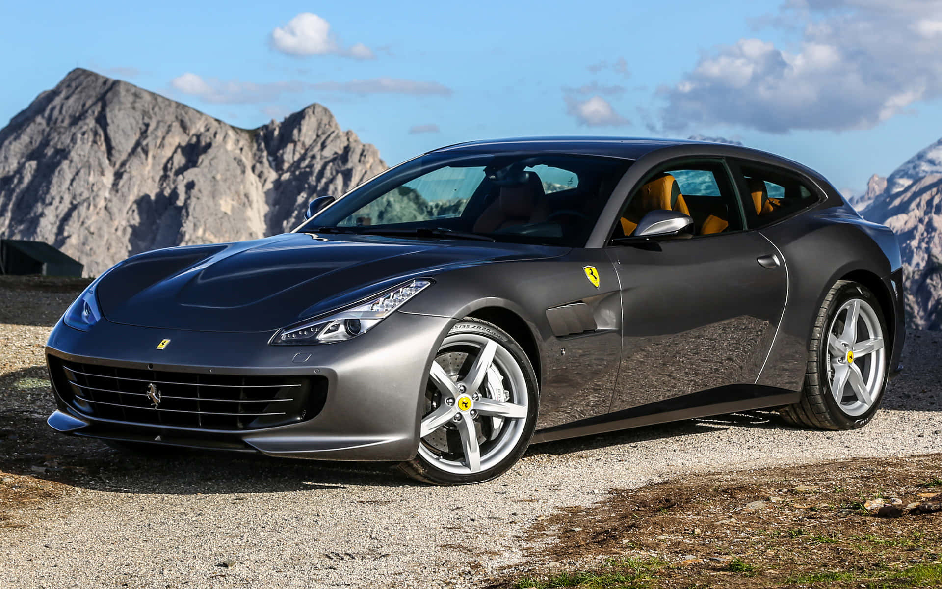 Ferrari Gtc4lusso 桌布 壁紙 — 一輛時尚的磨砂灰色法拉利 GTC4Lusso 停泊在碎石山路，背景是崎嶇的山峰和藍天。