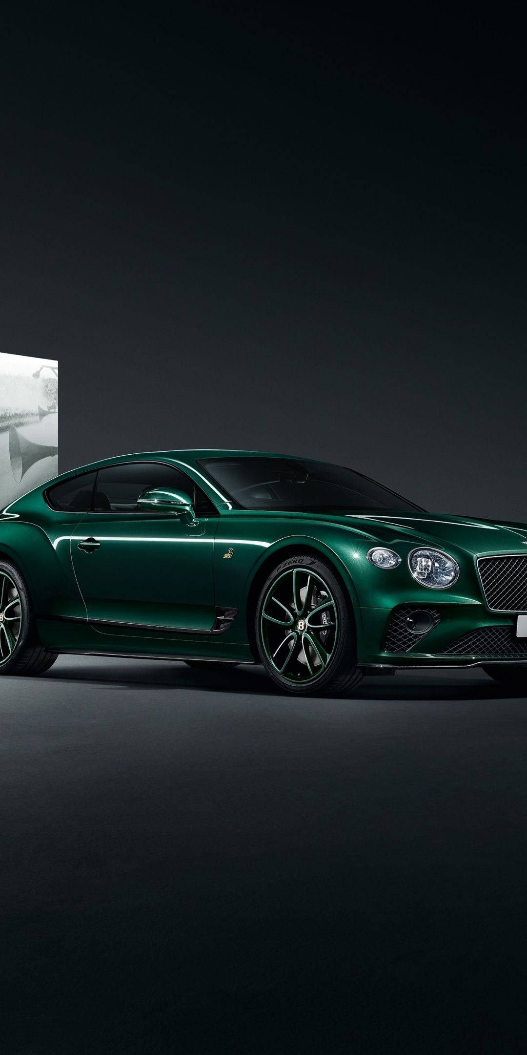 手機 桌布 壁紙 — 一輛時尚的祖母綠賓利 Continental GT 轎跑車在攝影棚燈光下閃耀，背景為深色極簡風格。