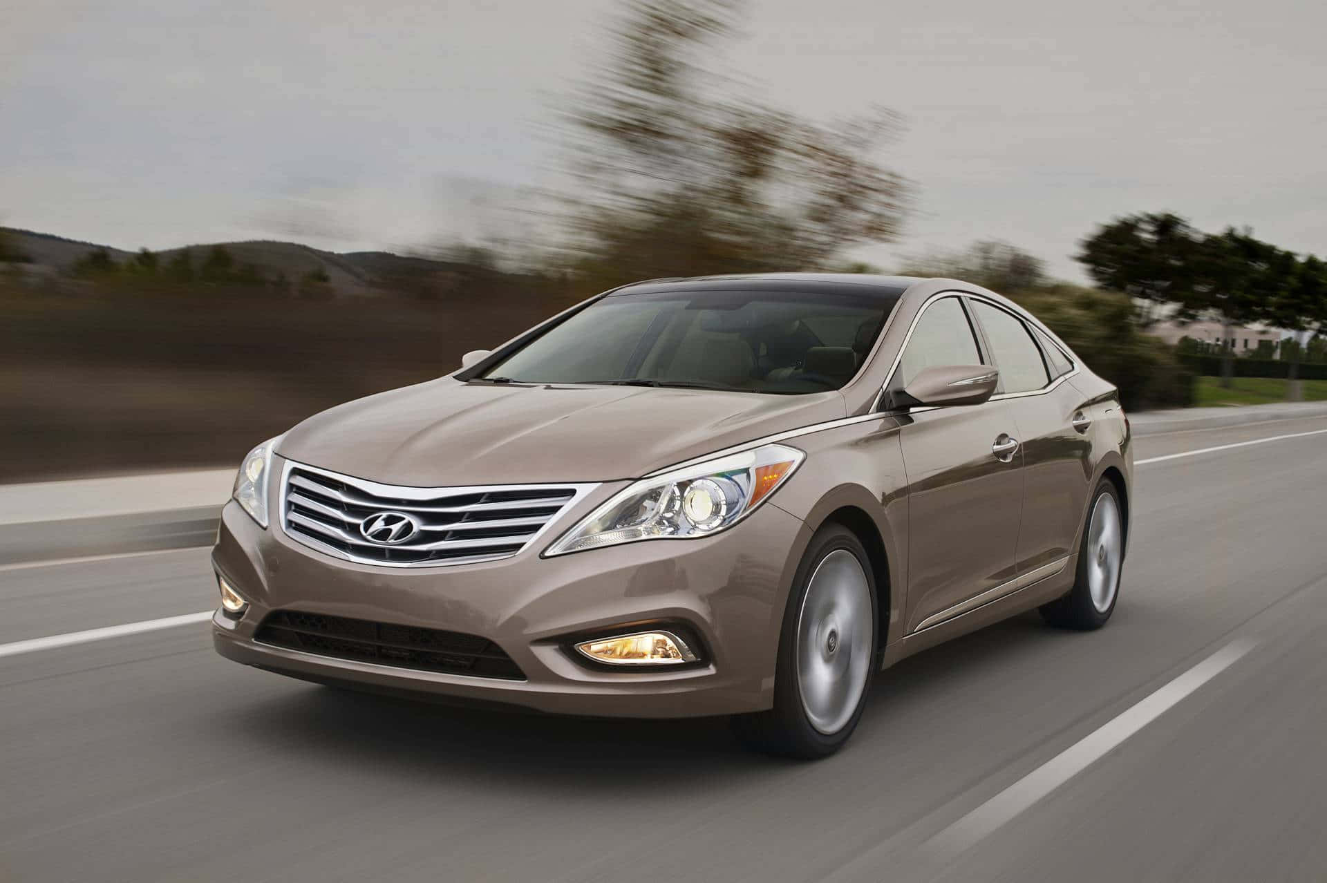 Hyundai Azera 桌布 壁紙 — 一輛時尚的米色現代轎車在高速公路上疾馳，背景是模糊的樹木和山丘。