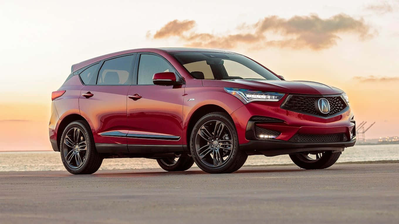 Acura Rdx 桌布 壁紙 — 一輛時尚的紅色Acura SUV停泊在日落時分的海岸公路上，溫暖的金色光線反射在其拋光表面上。