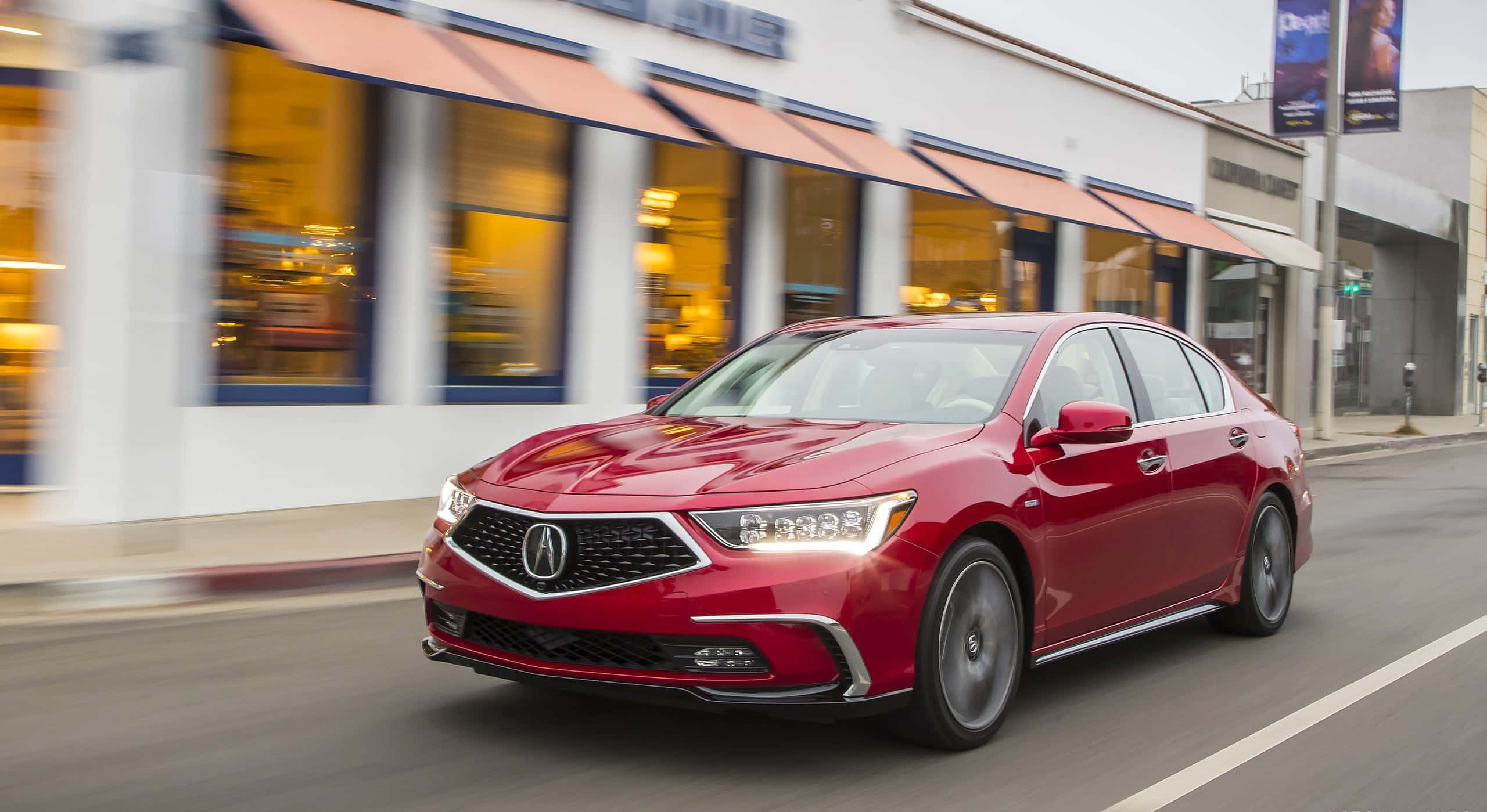 Acura Rlx 桌布 壁紙 — 一輛時尚的紅色Acura轎車在街道上行駛，背景中模糊的商店櫥窗散發著溫暖的光芒。