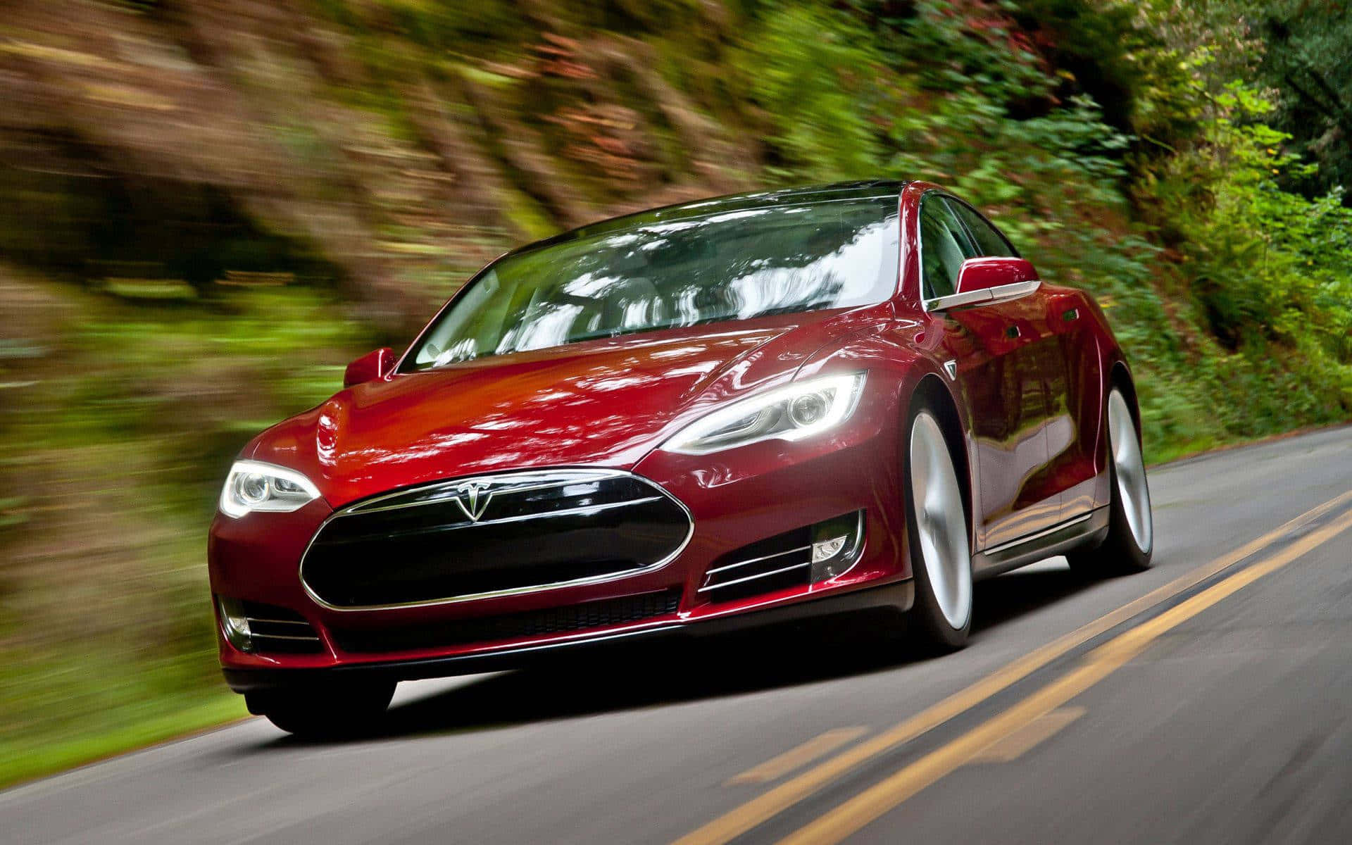 tesla 桌布 壁紙 — 一輛時尚的紅色Tesla Model S在蜿蜒的林間道路上疾馳，綠色樹葉呈現動態模糊效果。