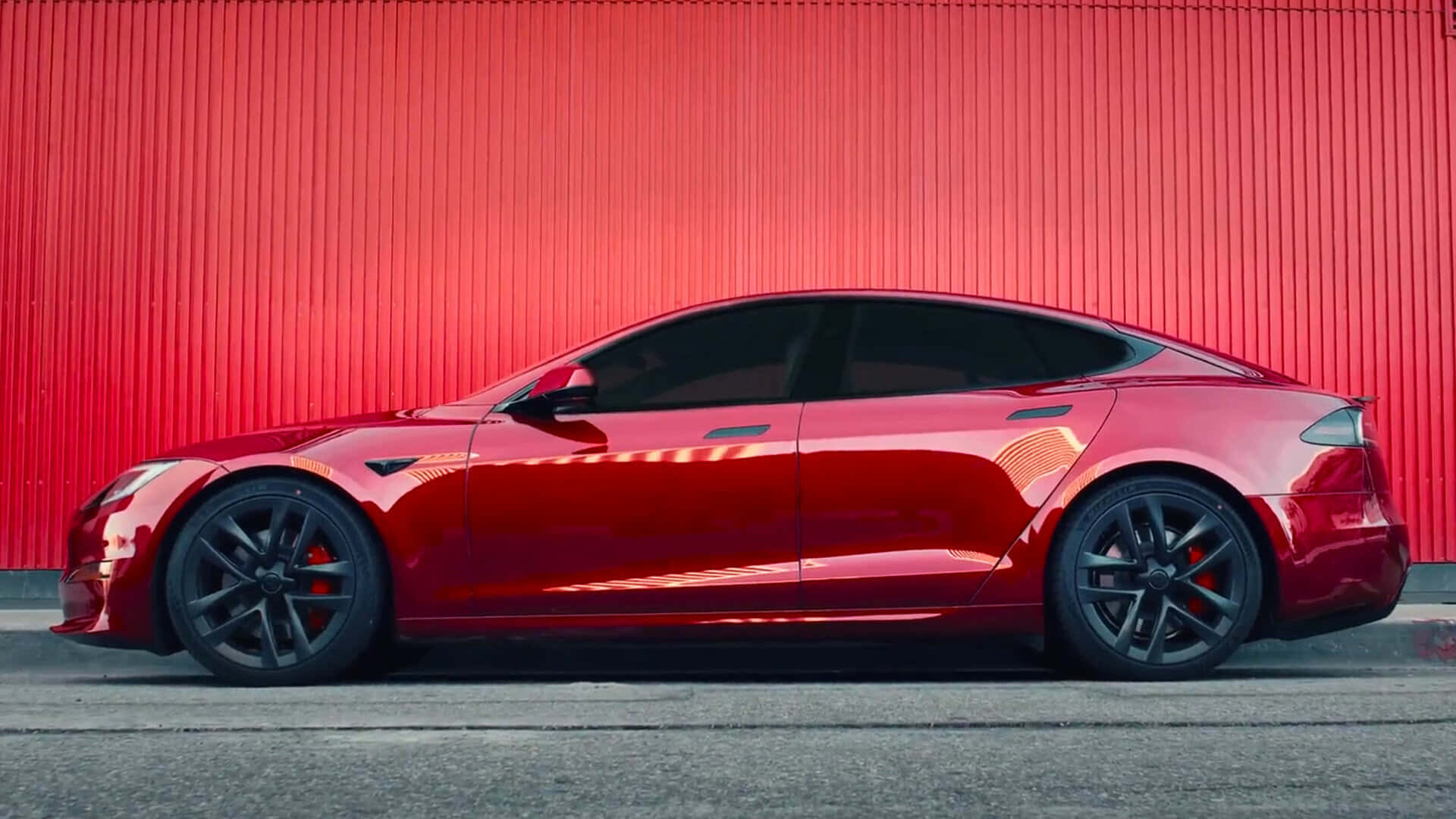tesla 桌布 壁紙 — 一輛時尚的紅色Tesla Model S跑車停在一面充滿活力的紅色波紋金屬牆前。