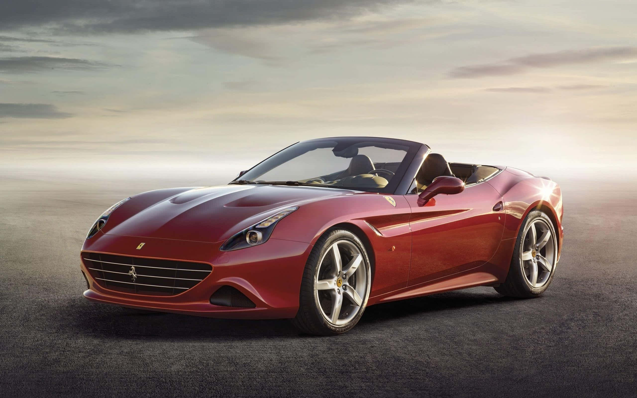 Ferrari California T 桌布 壁紙 — 一輛時尚的紅色法拉利敞篷車在開闊的瀝青路上，在柔和的金色夕陽下閃閃發光。