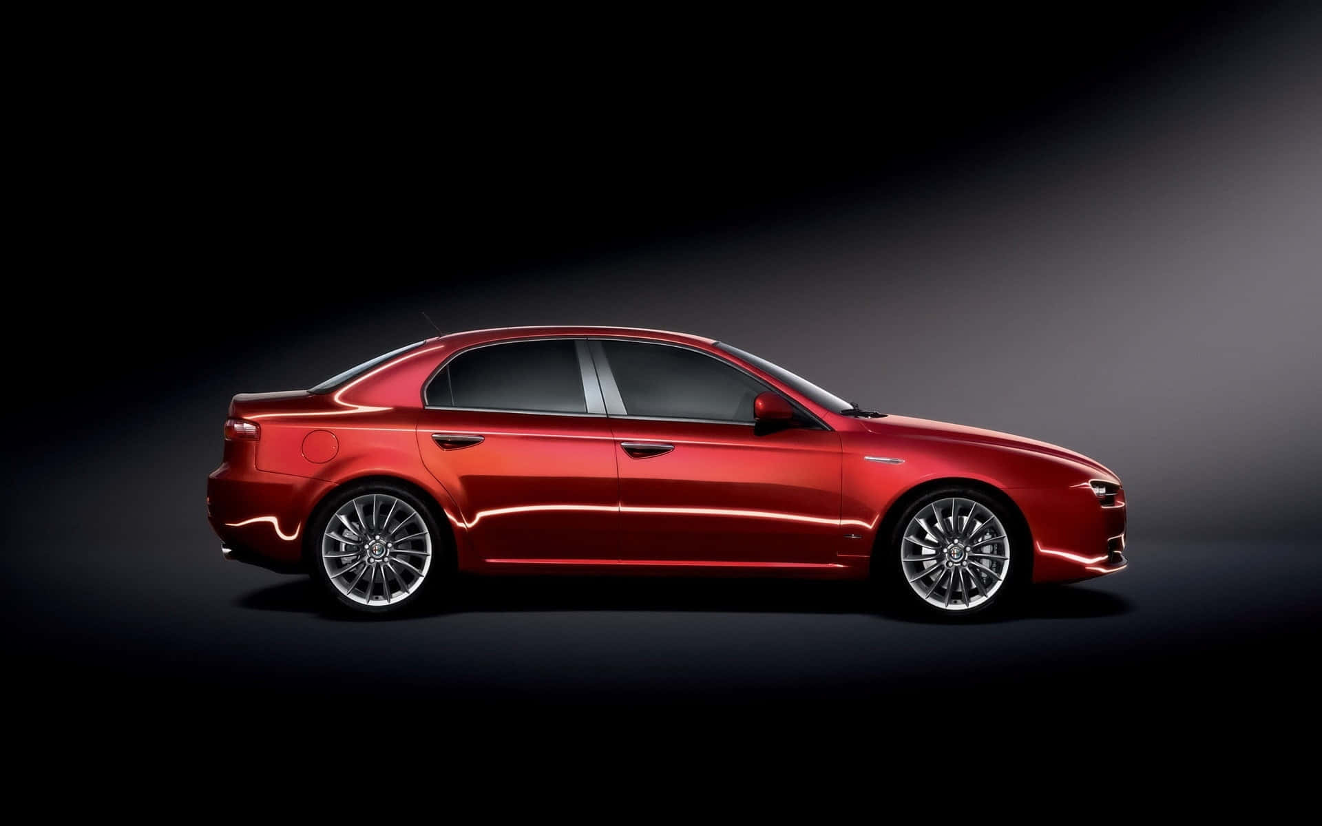 Alfa Romeo 159 桌布 壁紙 — 一輛時尚的紅色轎車在攝影棚燈光下閃閃發光，以深色漸變背景襯托出其空氣動力學輪廓和合金輪圈。