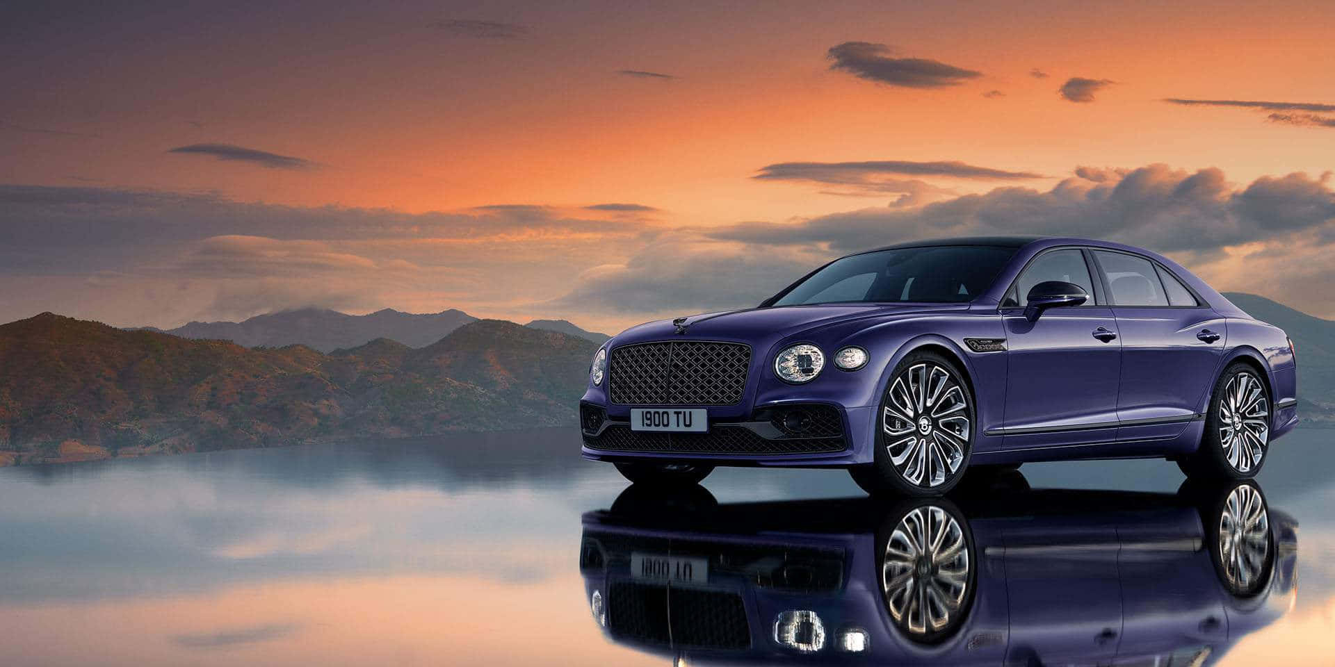 Bentley Flying Spur 桌布 壁紙 — 一輛時尚的紫色賓利轎車完美地倒映在平靜的水面上，背景是 vibrant 的橙色日落天空和遠山。