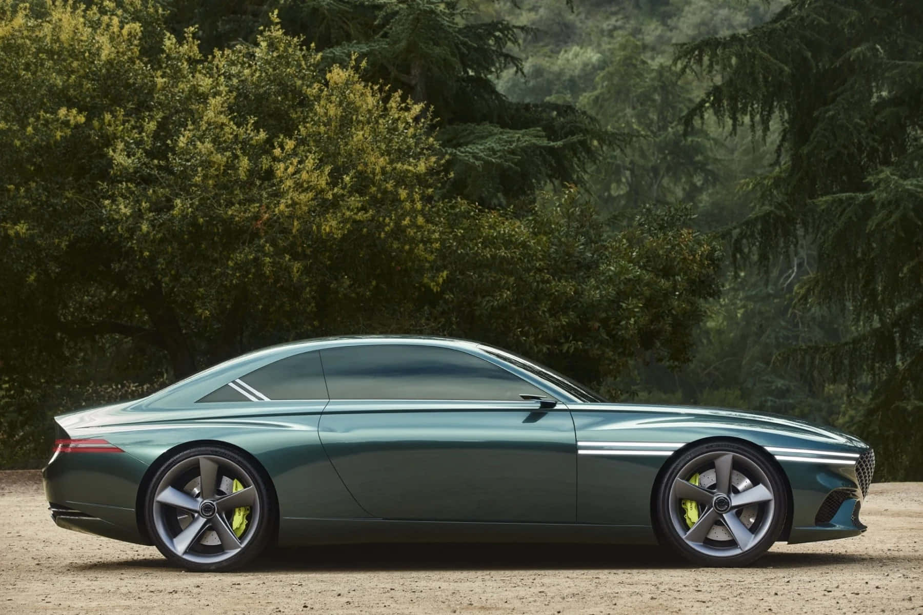Genesis X Concept 桌布 壁紙 — 一輛時尚的綠色概念車，帶有黃色制動卡鉗，停在泥土上，旁邊是茂密的綠樹。