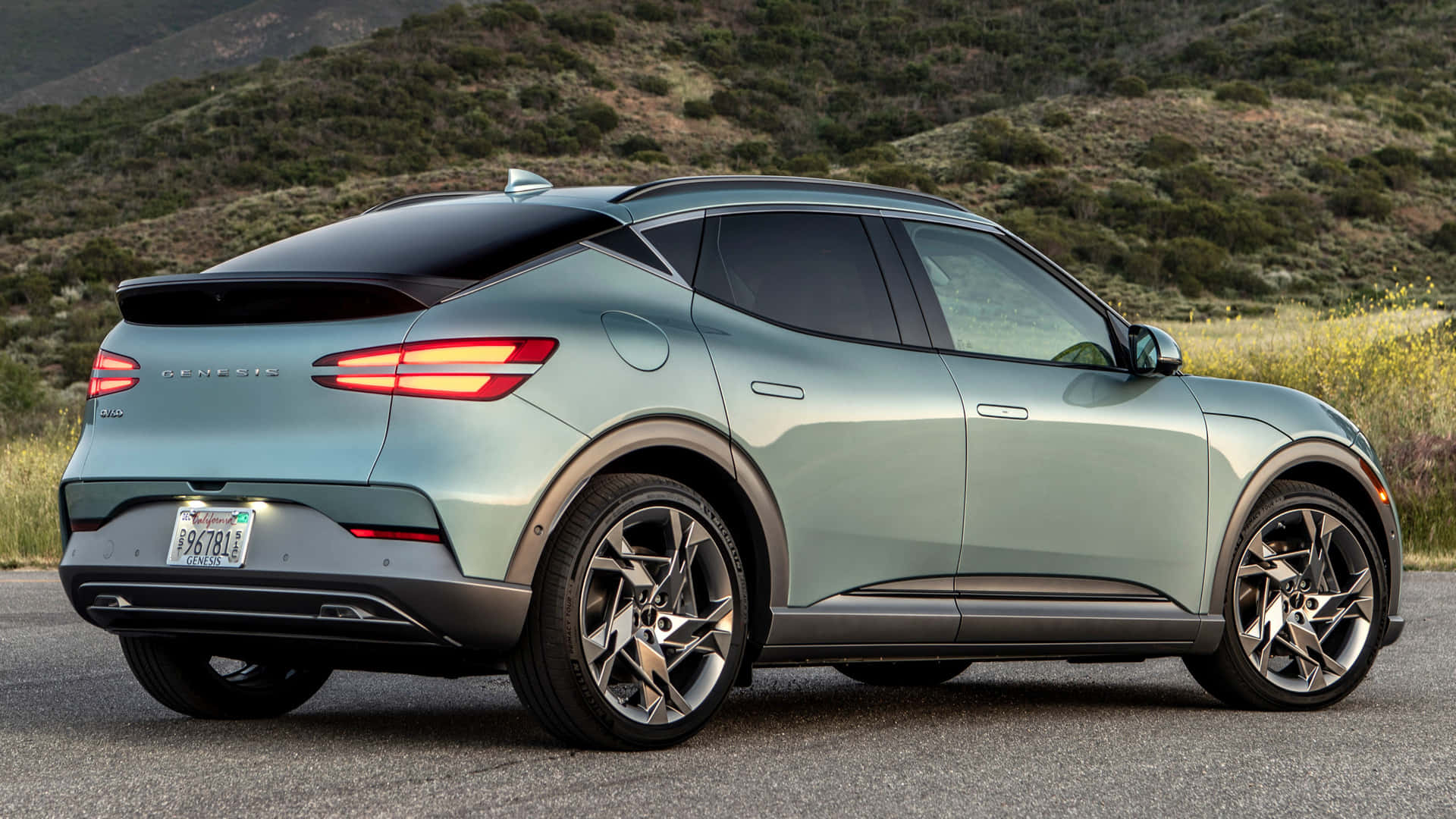 Genesis Gv60 桌布 壁紙 — 一輛時尚的薄荷綠色 Genesis GV60 電動 SUV 停在瀝青路上，背景是山丘和野花。