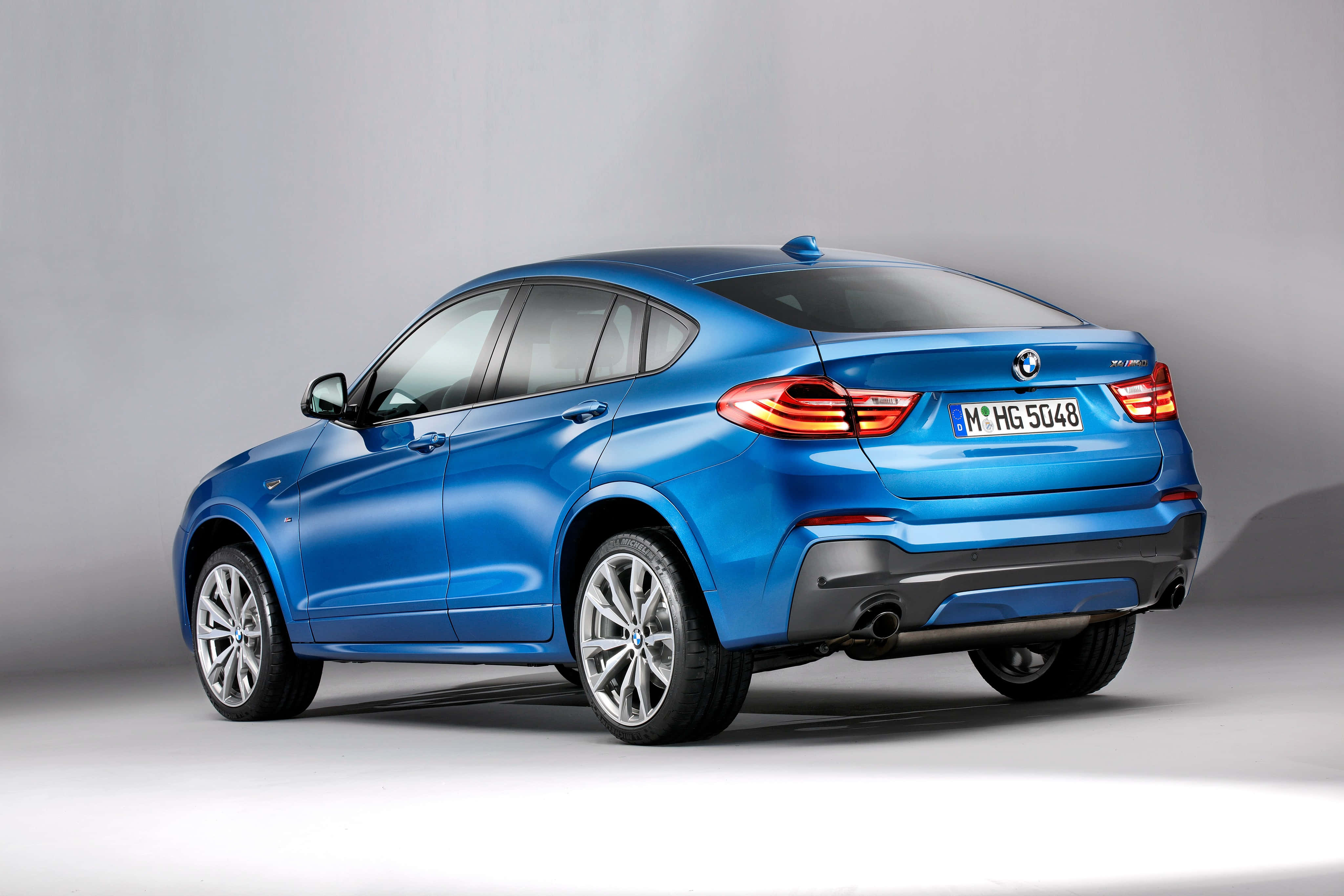 Bmw X4 桌布 壁紙 — 一輛時尚的藍色BMW X4轎跑SUV，在工作室燈光下展示，帶有發光的尾燈和鍍鉻輪圈。