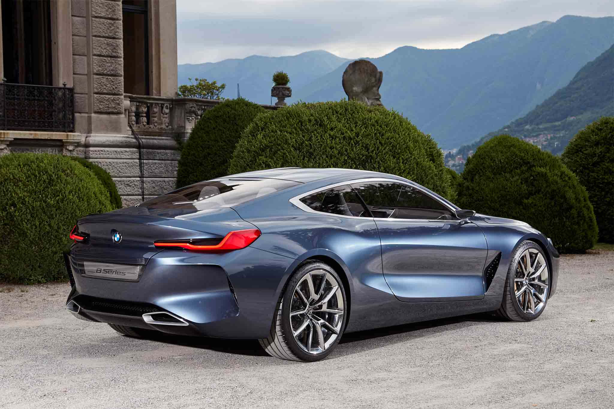 Bmw 8 Series 桌布 壁紙 — 一輛時尚的藍色BMW概念車停在碎石路上，前方是一座宏偉的石砌別墅，修剪整齊的樹籬和遠處的山脈在陰天之下。