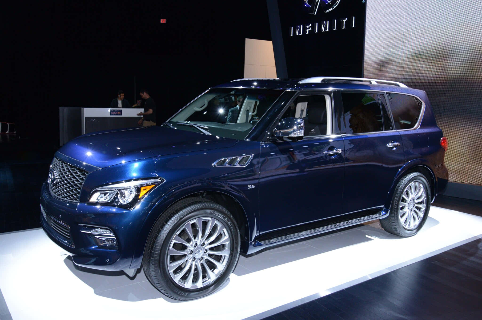 Infiniti Qx80 桌布 壁紙 — 一輛時尚的藍色Infiniti QX80 SUV在車展的白色平台上，在明亮的燈光下閃閃發光。