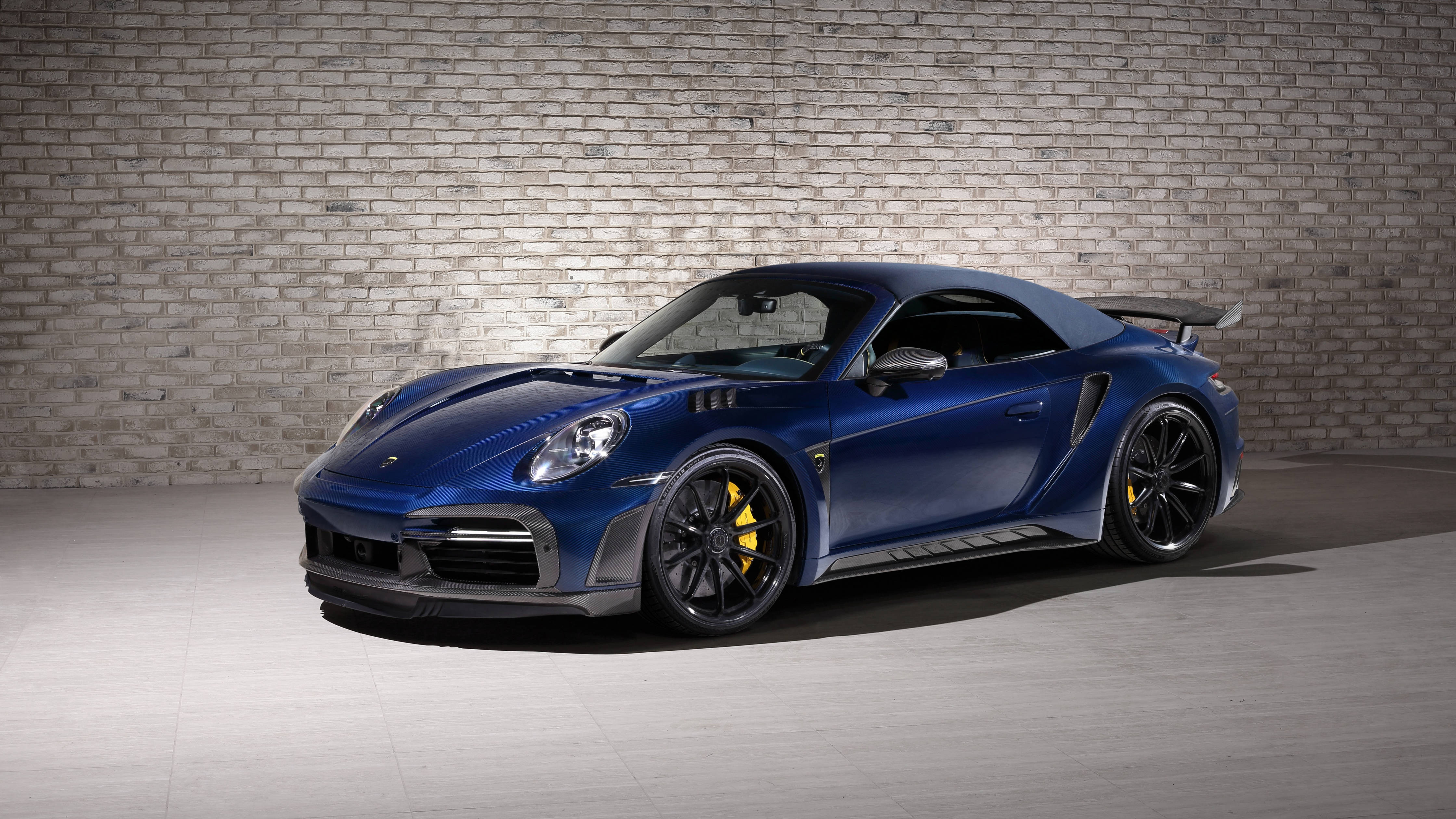 4K 桌布 壁紙 — 一輛時尚的藍色保時捷911 Turbo S，配備黃色制動卡鉗，在極簡主義的工作室環境中，停在紋理灰色磚牆前。