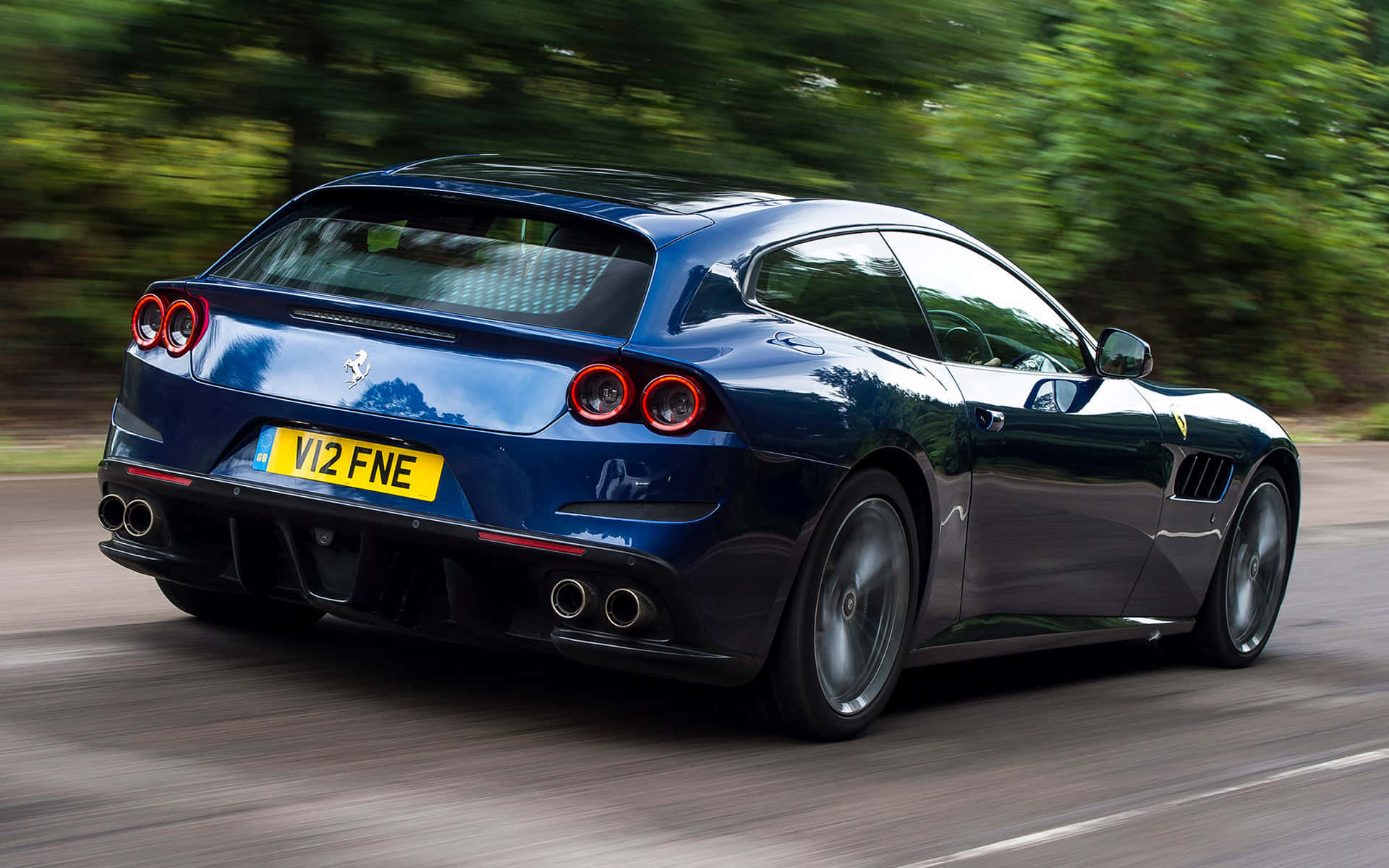 Ferrari Gtc4lusso 桌布 壁紙 — 一輛時尚的藍色法拉利FF在綠樹成蔭的道路上飛馳，動態模糊凸顯其力量與優雅。