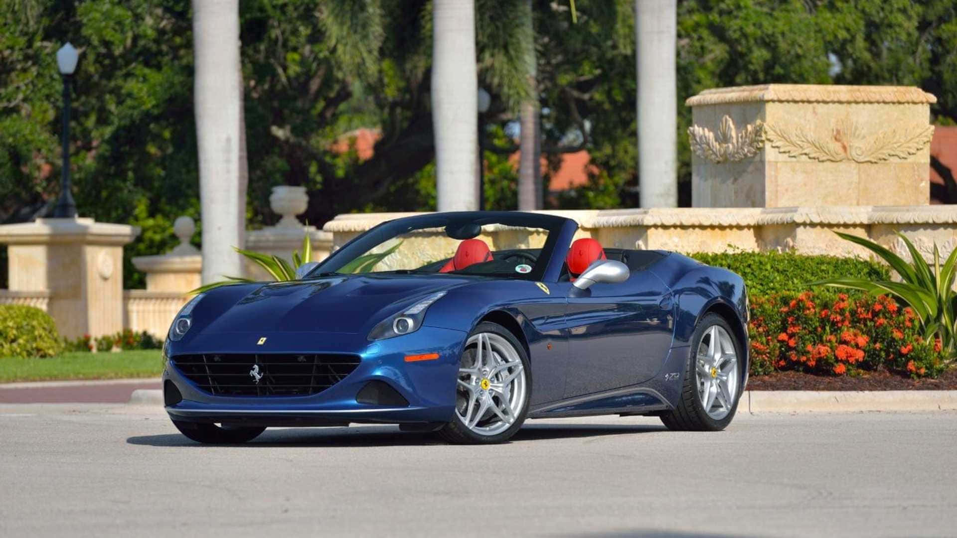 Ferrari California T 桌布 壁紙 — 一輛時尚的藍色法拉利敞篷車，配備紅色座椅，停在陽光明媚的街道上，旁邊有棕櫚樹和華麗的石柱。